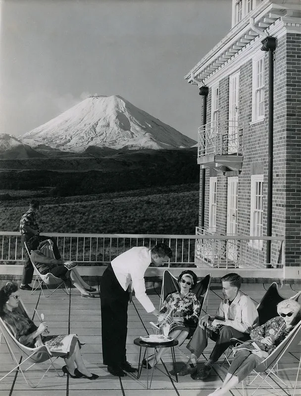 A waiter serving drinks on a balcony in front of a mountain