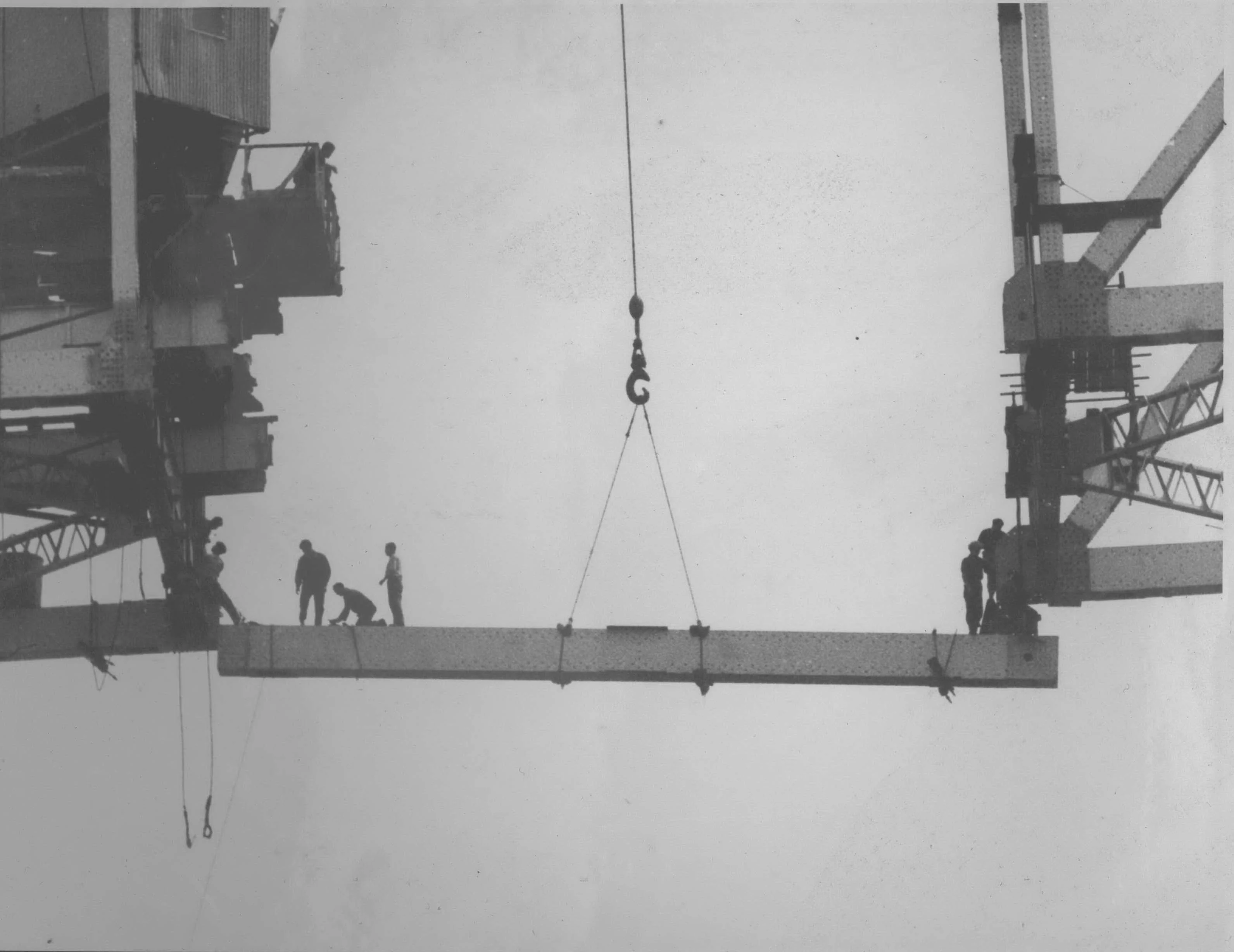 Male workers standing unassisted on a girder as it's being fitted.