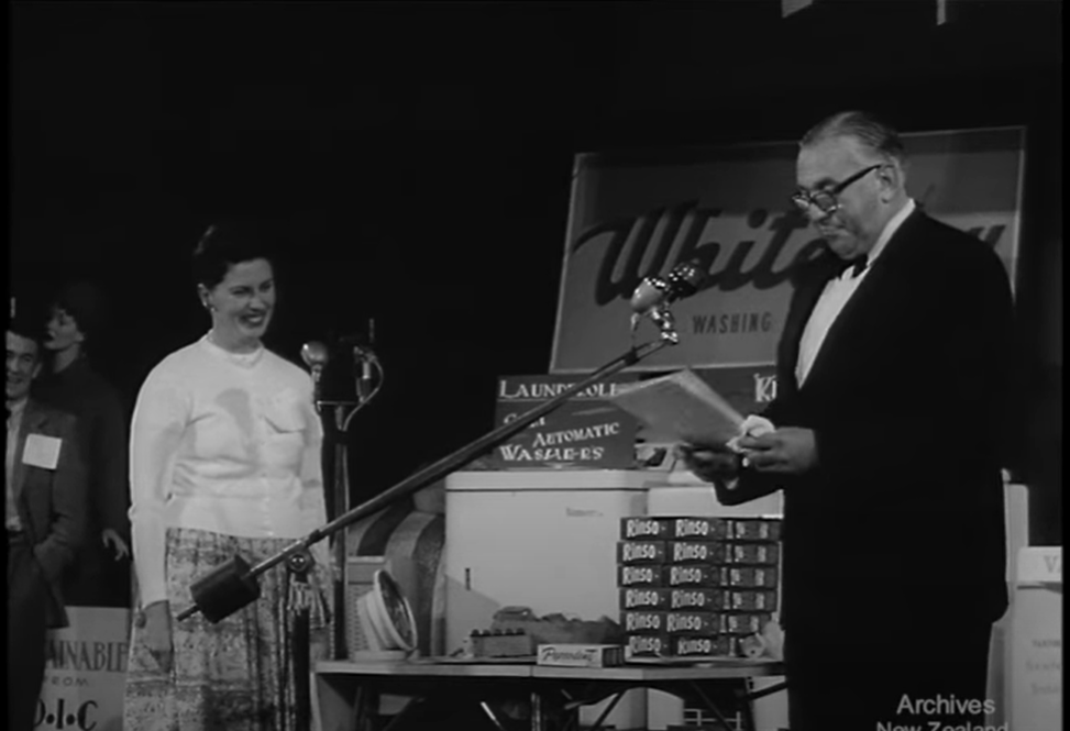 A still from 'Pictorial Parade 86 - Inside the Bag'. A game show host reads a question while the contestant smiles.