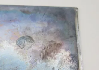 Photograph of the top-right corner of a piece of coloured glass, marked with two brown fingerprints.