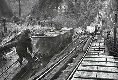 Person pushing coal carts along railway tracks at a mine.