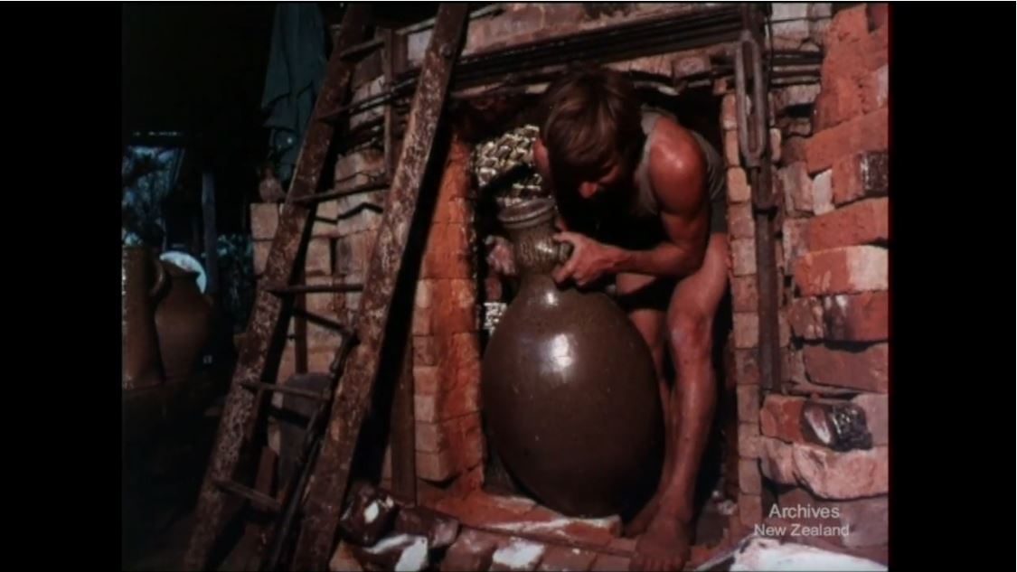Barry Brickell carries a large urn out of a brick kiln.