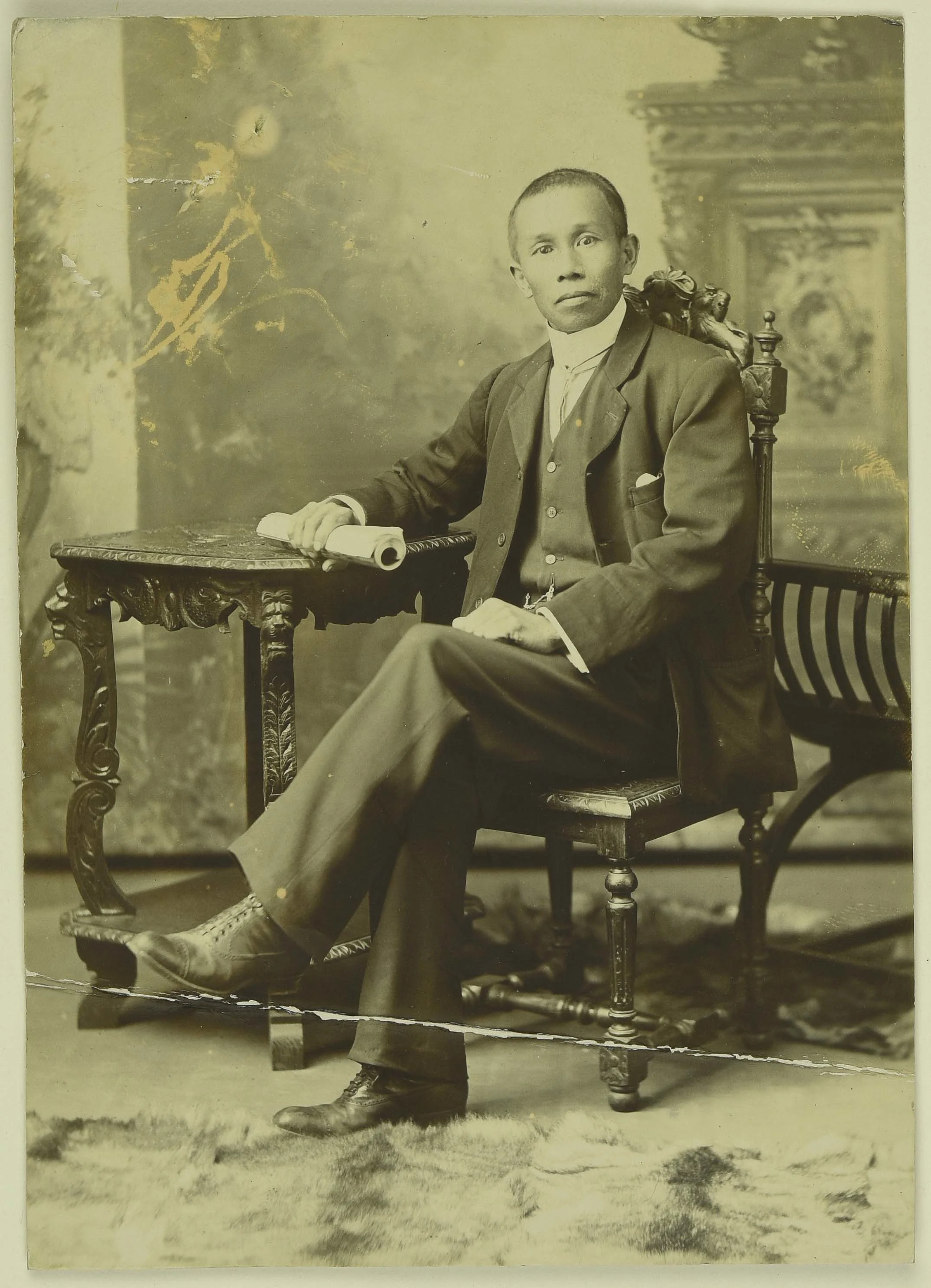 Sepia photo of a seated Chinese man resting his arm on a table.