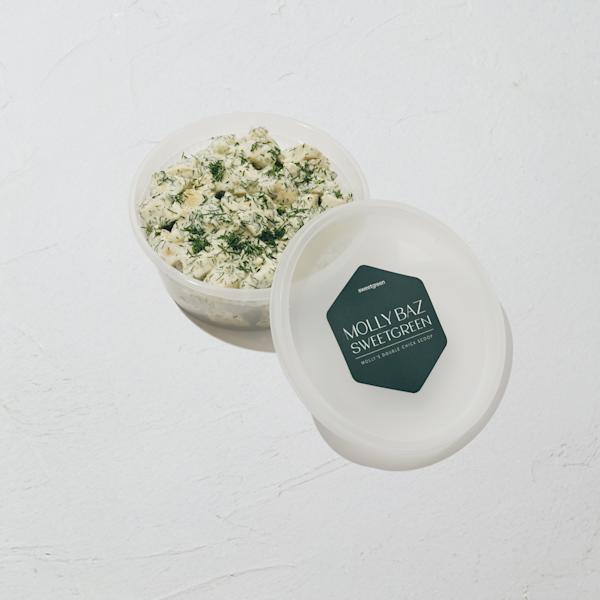 An open container of creamy chicken salad topped with fresh dill, next to its lid bearing a dark green sweetgreen label reading "Molly Baz x sweetgreen — Molly's Double Chick Scoop."