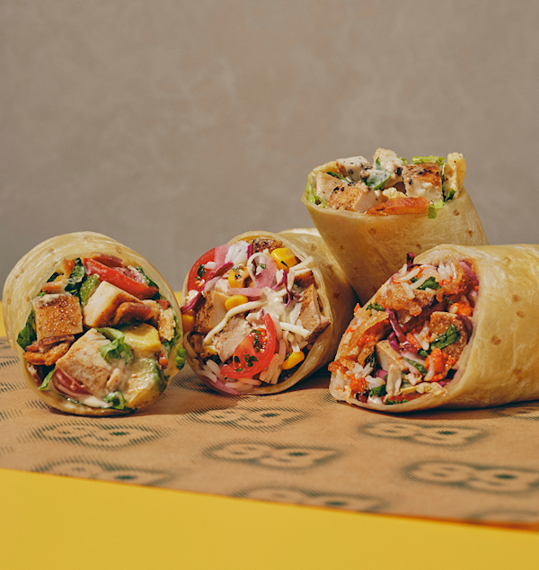 Close up image of all four new sweetgreen wraps laying on branded sweetgreen wraps paper on a yellow table.