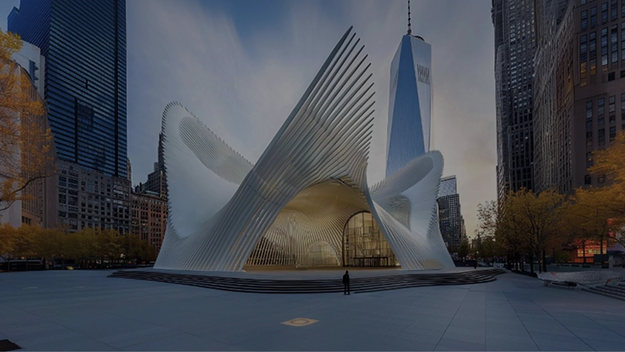 The Oculus in New York City in the center of a plaza surrounded by autumn trees and skyscrapers with One World Trade Center in the background.