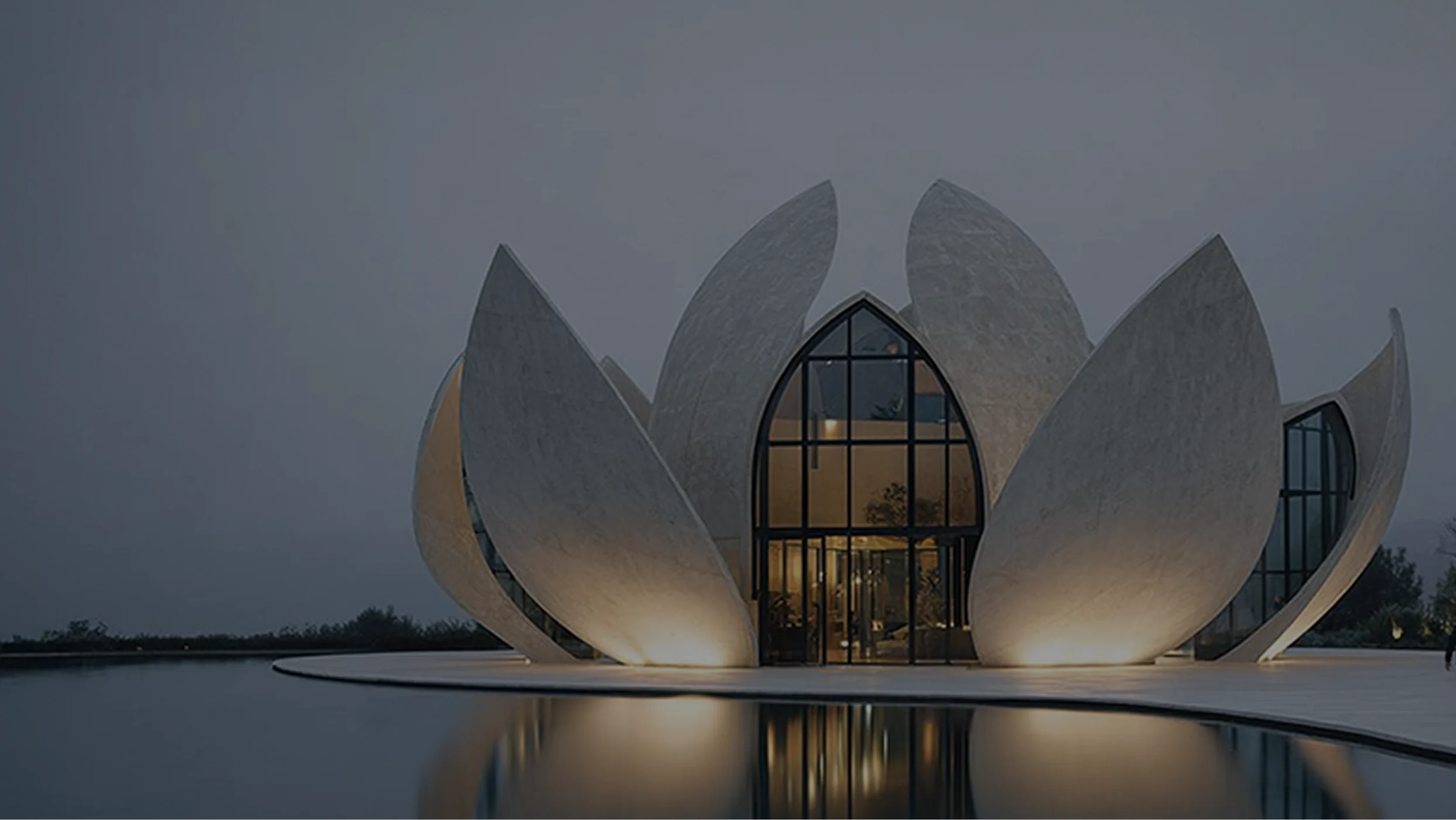 Edificio moderno a forma di fiore di loto bianco illuminato al crepuscolo, riflesso sulla superficie di uno specchio d'acqua.