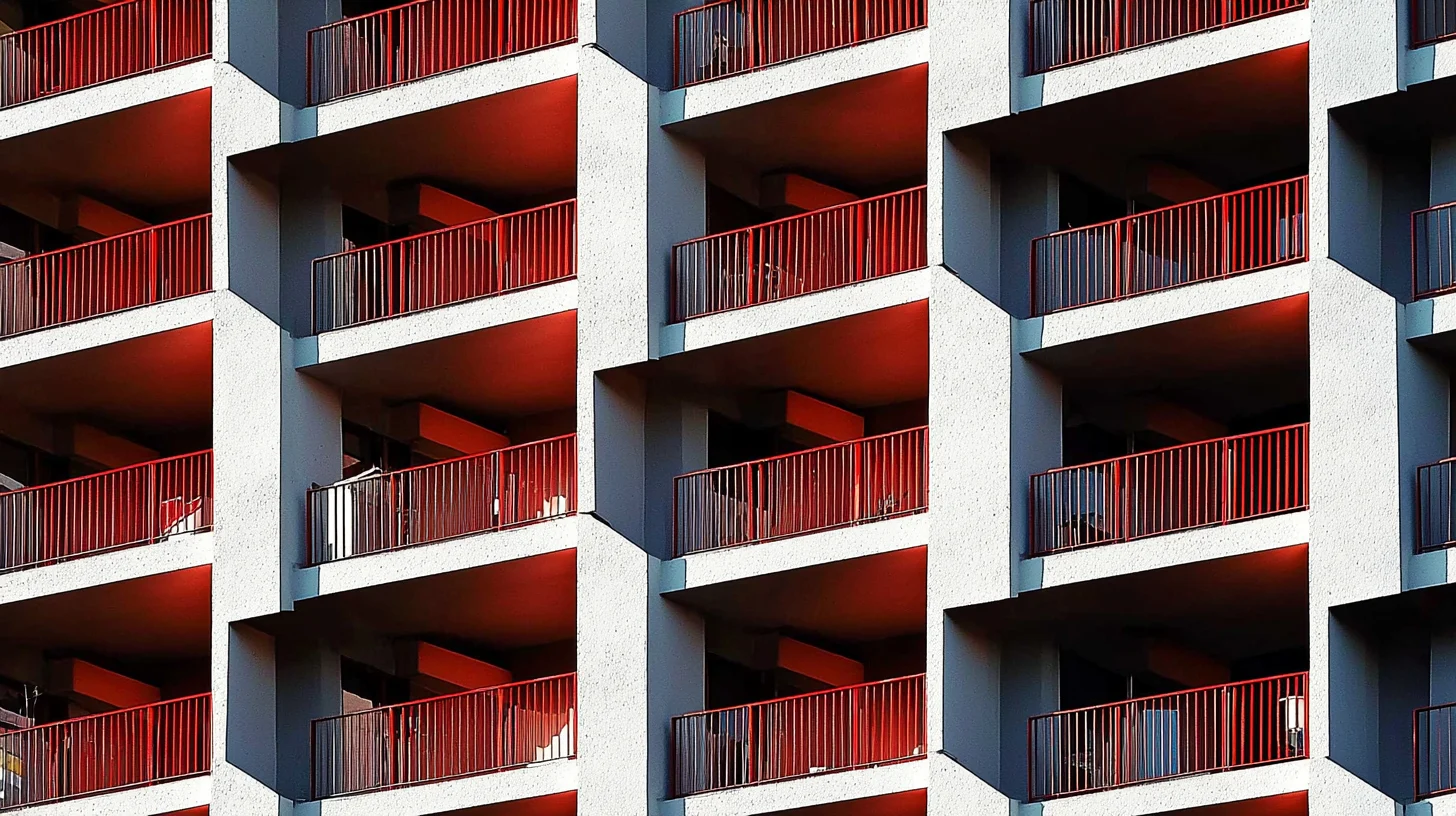 Facciata moderna di un hotel con balconi geometrici in cemento e ringhiere rosse ripetute in serie.