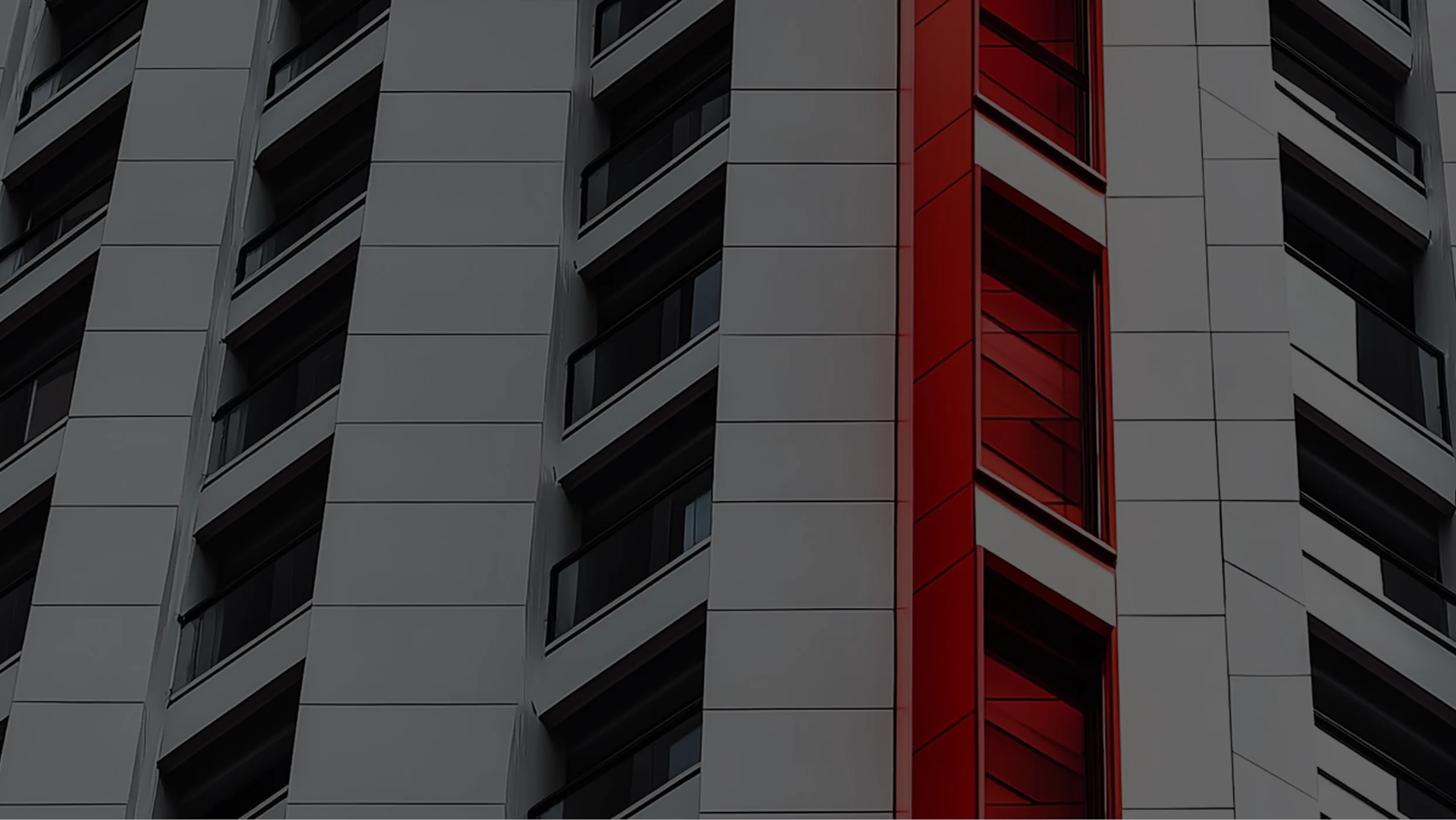 Geometric architectural close-up of a modern building facade. White paneled cladding and dark balconies with railings. A central vertical column of windows and glossy red cladding panels creates a striking contrast.