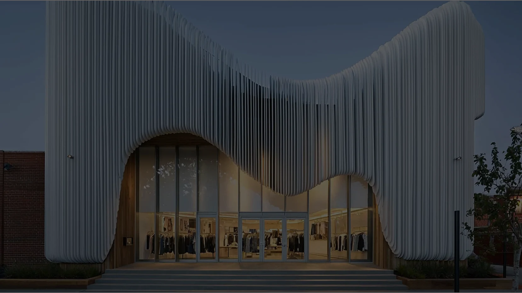 A modern, glass-walled fashion boutique set in a desert landscape at sunset.
