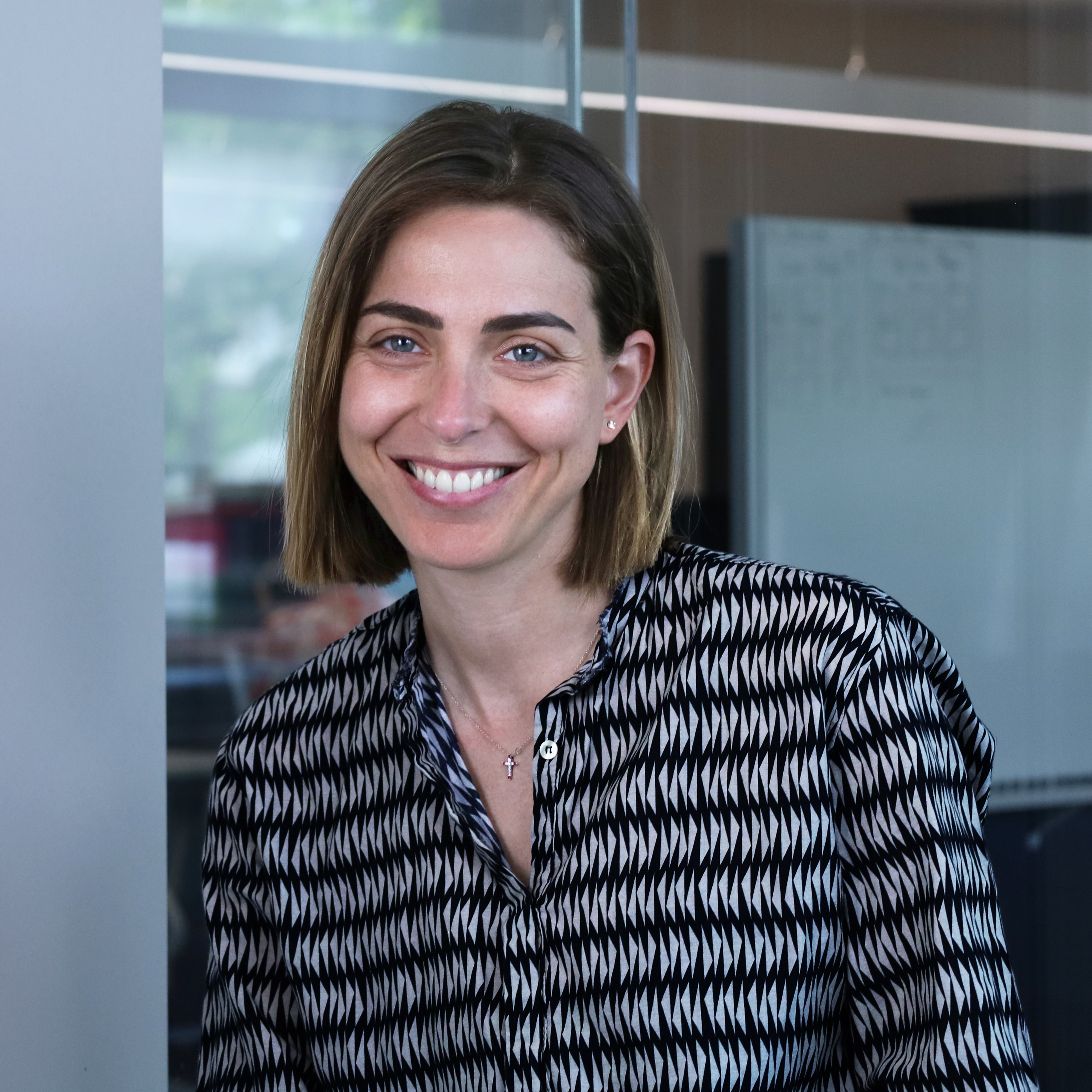 Professional portrait of Martina Visani, who works at Redify as a Business Consultant, featuring a smiling woman with brown bob hair, blue eyes and a black and white geometric shirt in a modern office.