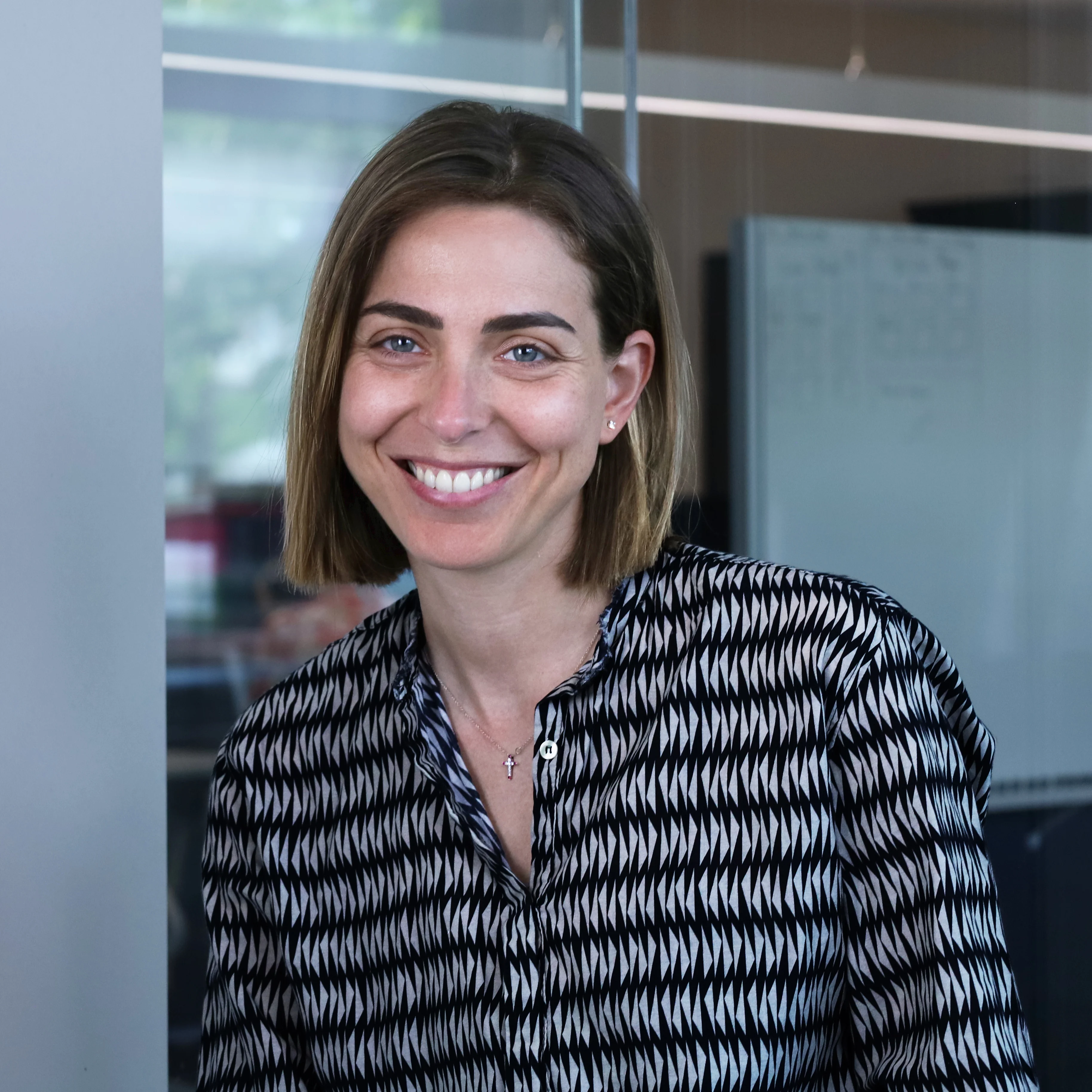 Professional portrait of Martina Visani, who works at Redify as a Business Consultant, featuring a smiling woman with brown bob hair, blue eyes and a black and white geometric shirt in a modern office.