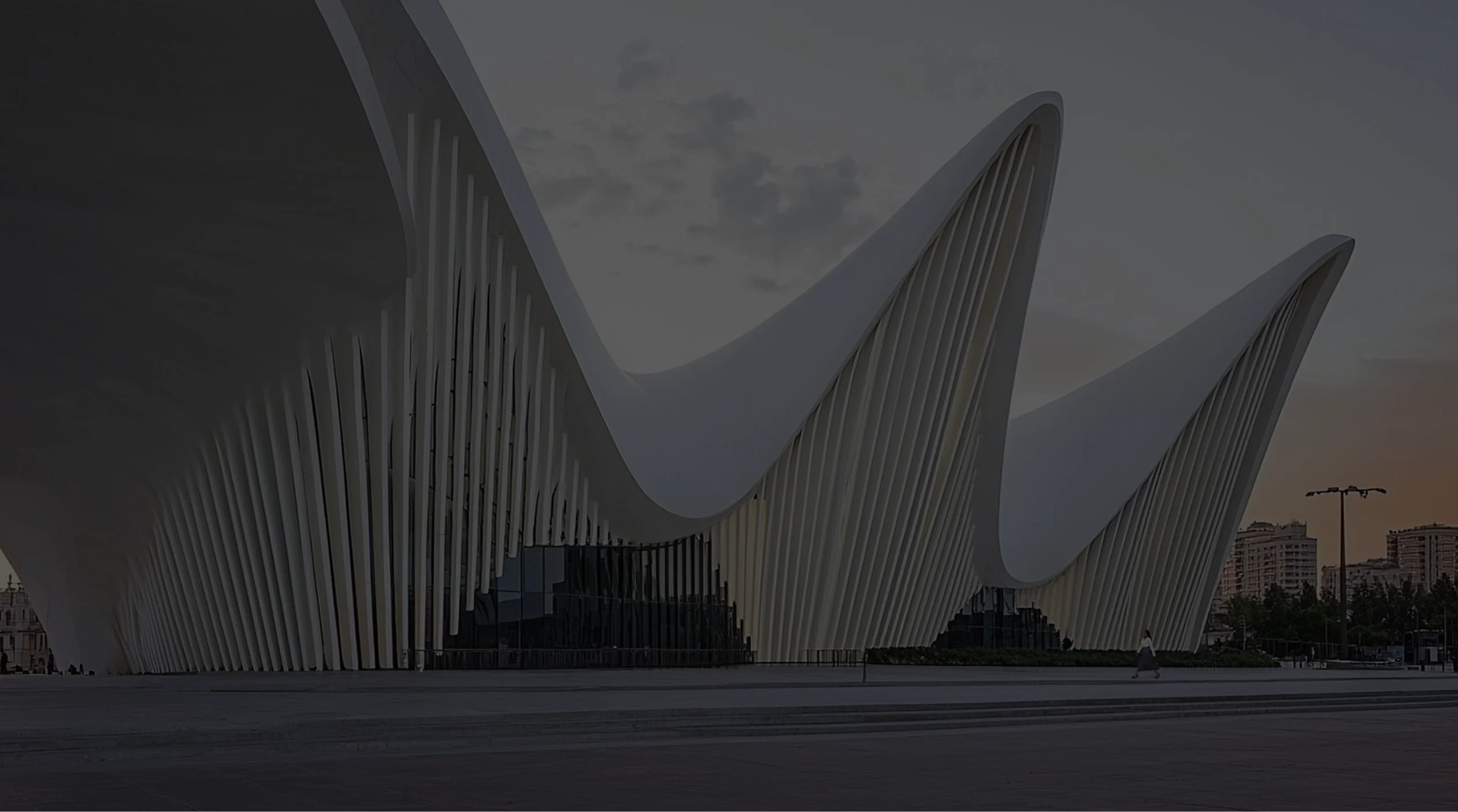 The modern architecture of the Heydar Aliyev Cultural Center in Baku, featuring a white facade with imposing flowing, curved, and undulating forms that stand out against the sunset sky.