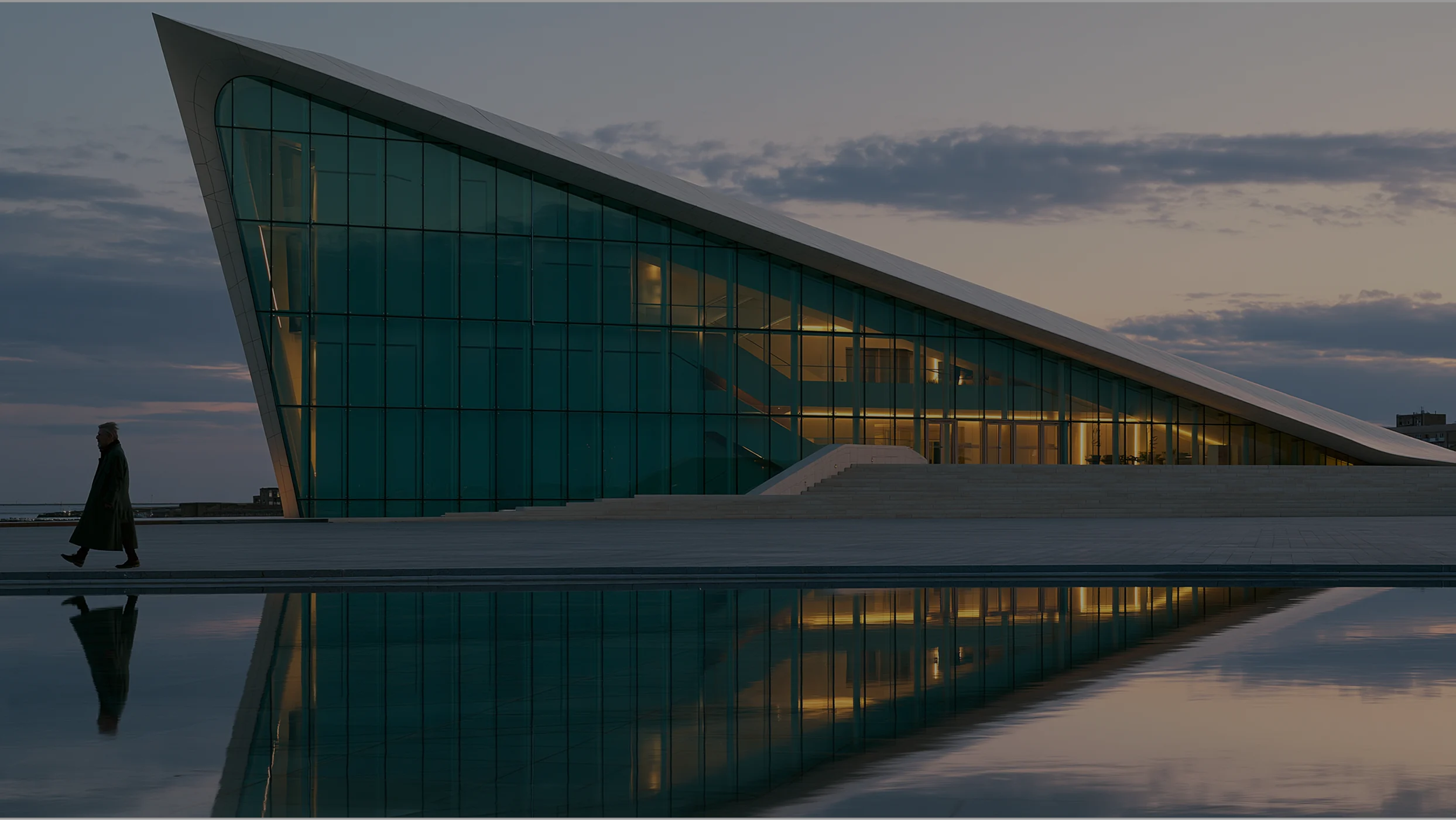Modern glass and marble building with a person in silhouette and their mirrored reflection in the water at sunset.
