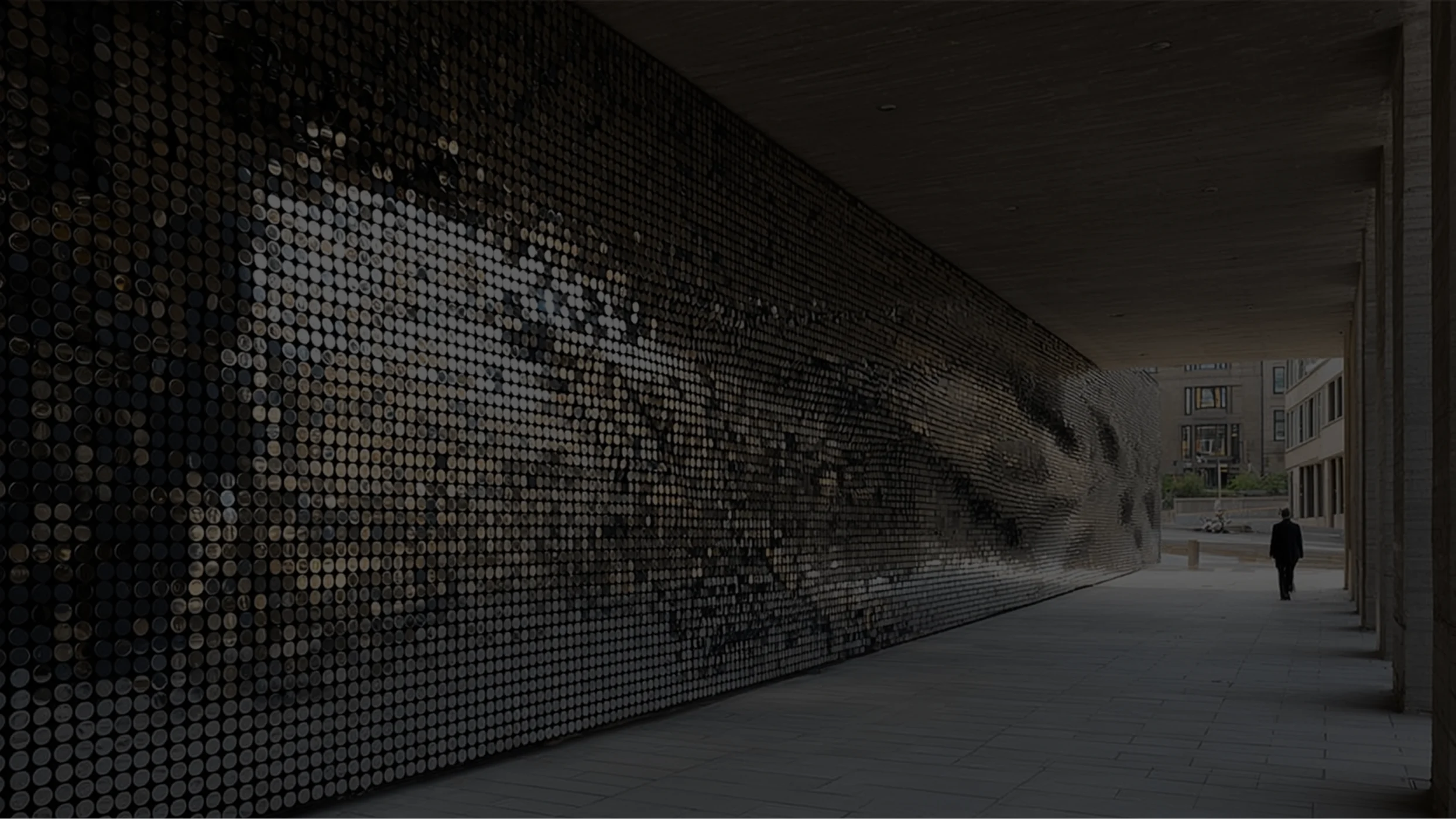 Decorative architectural wall with reflective pixelated metal discs inside a modern covered walkway.