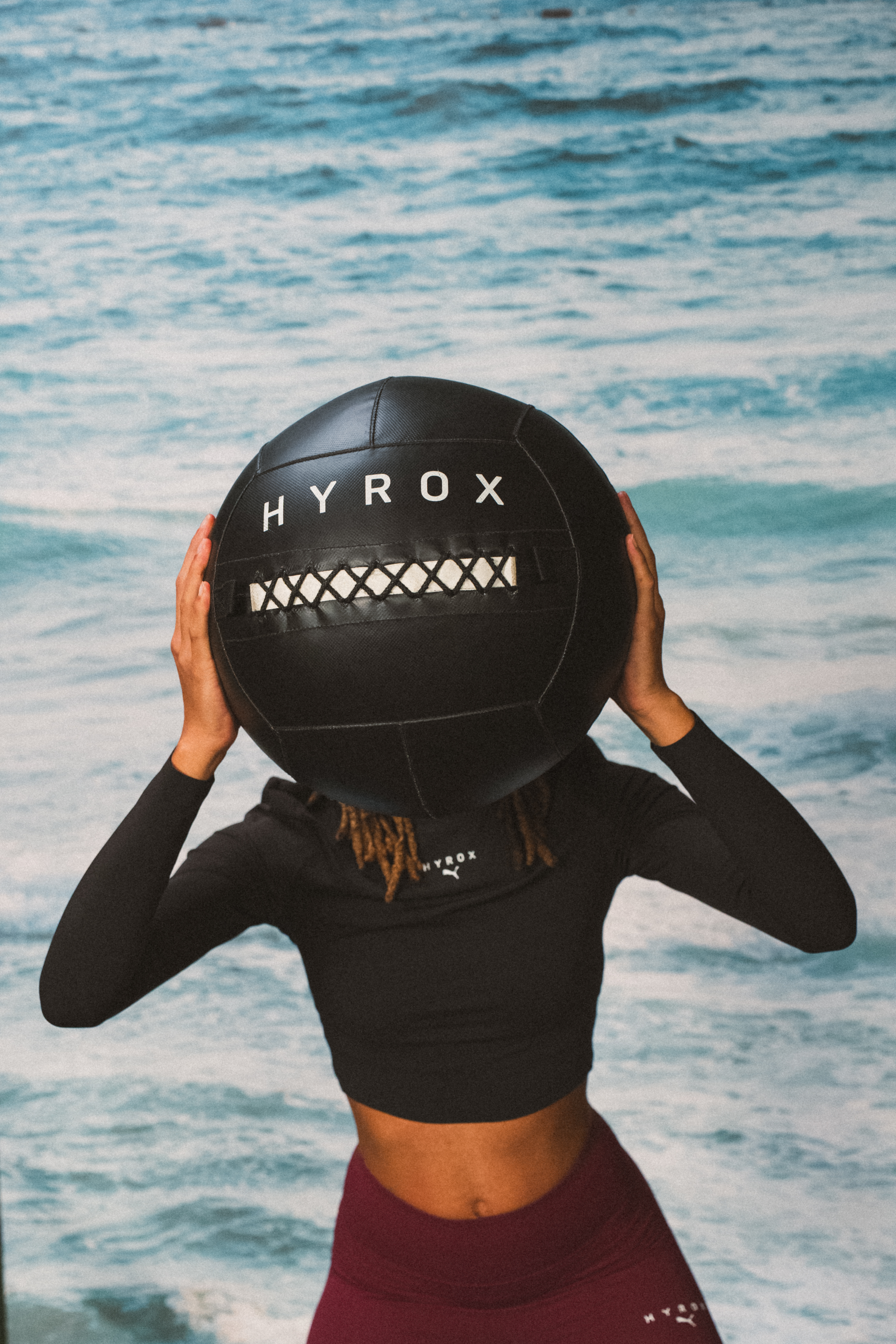Person holding large black Hyrox ball in front of blue background.