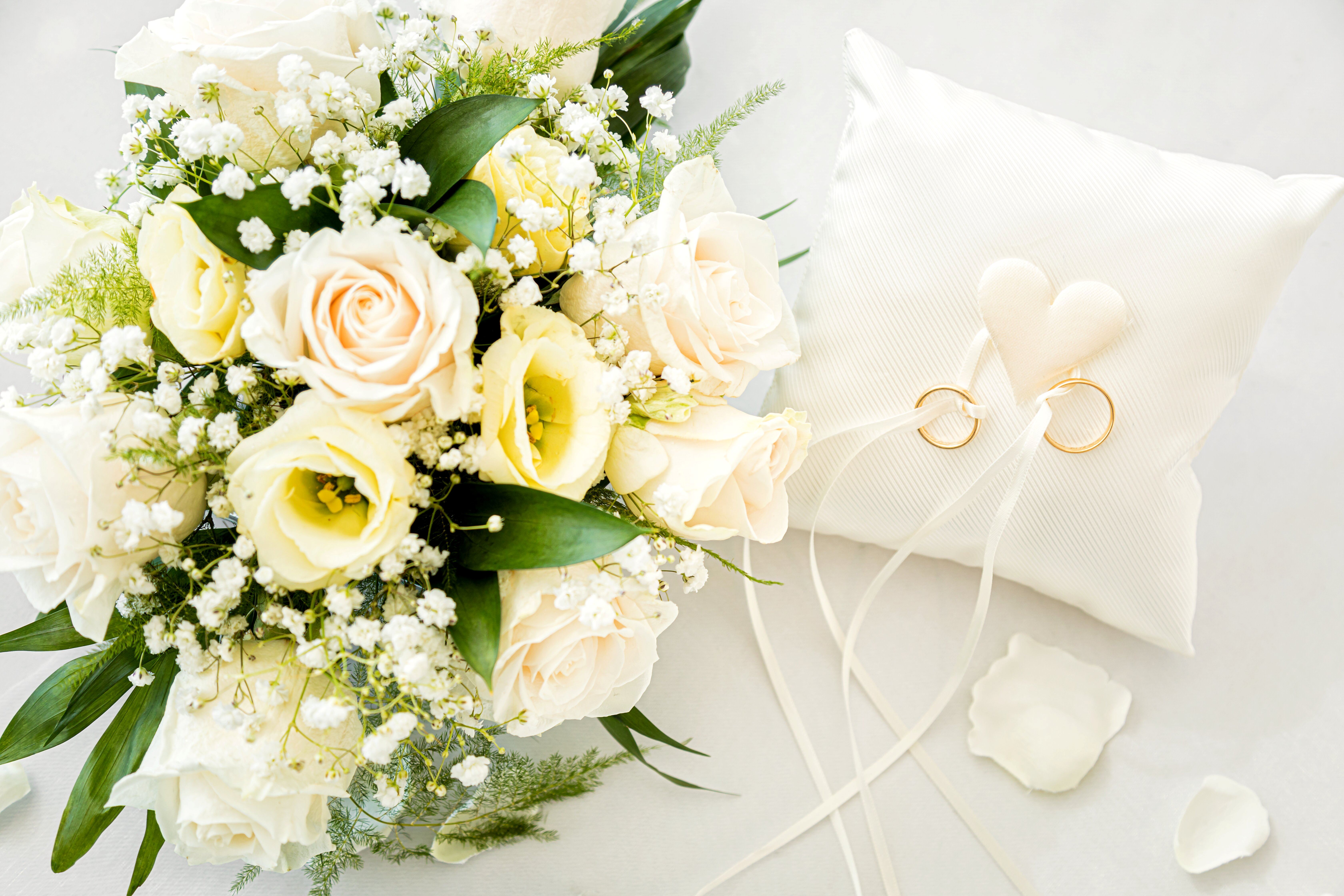 Brautstrauß mit weißen Rosen und Eheringe auf Kissen.
