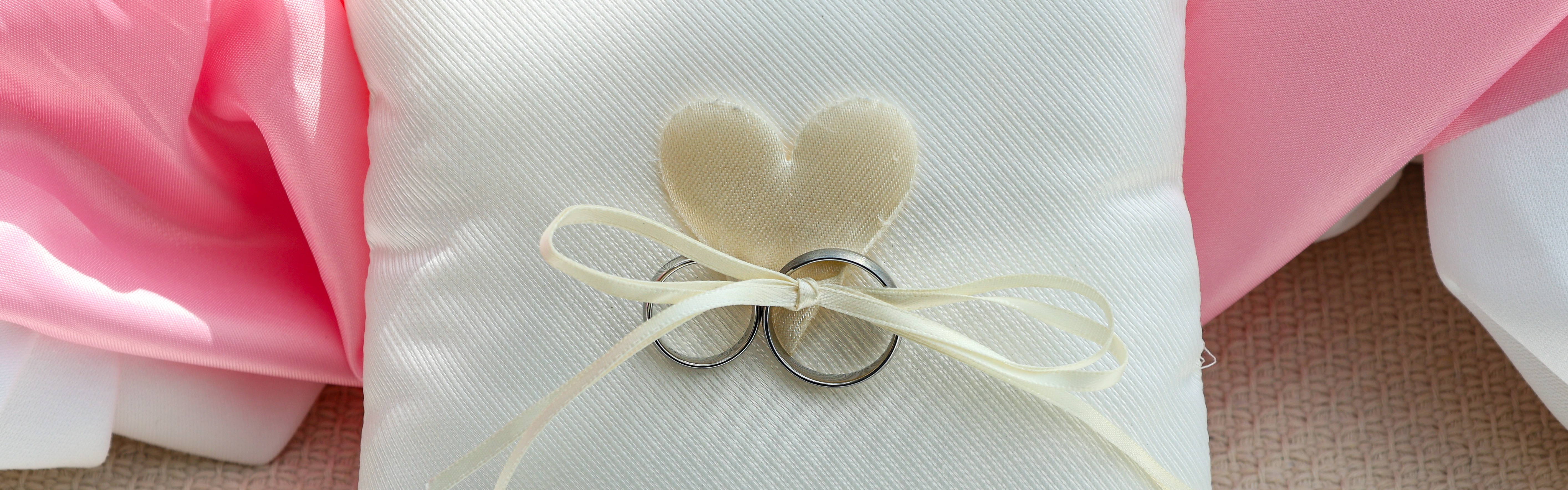 Weiße Kissen mit Ringen und Herz, rosa Hintergrund.