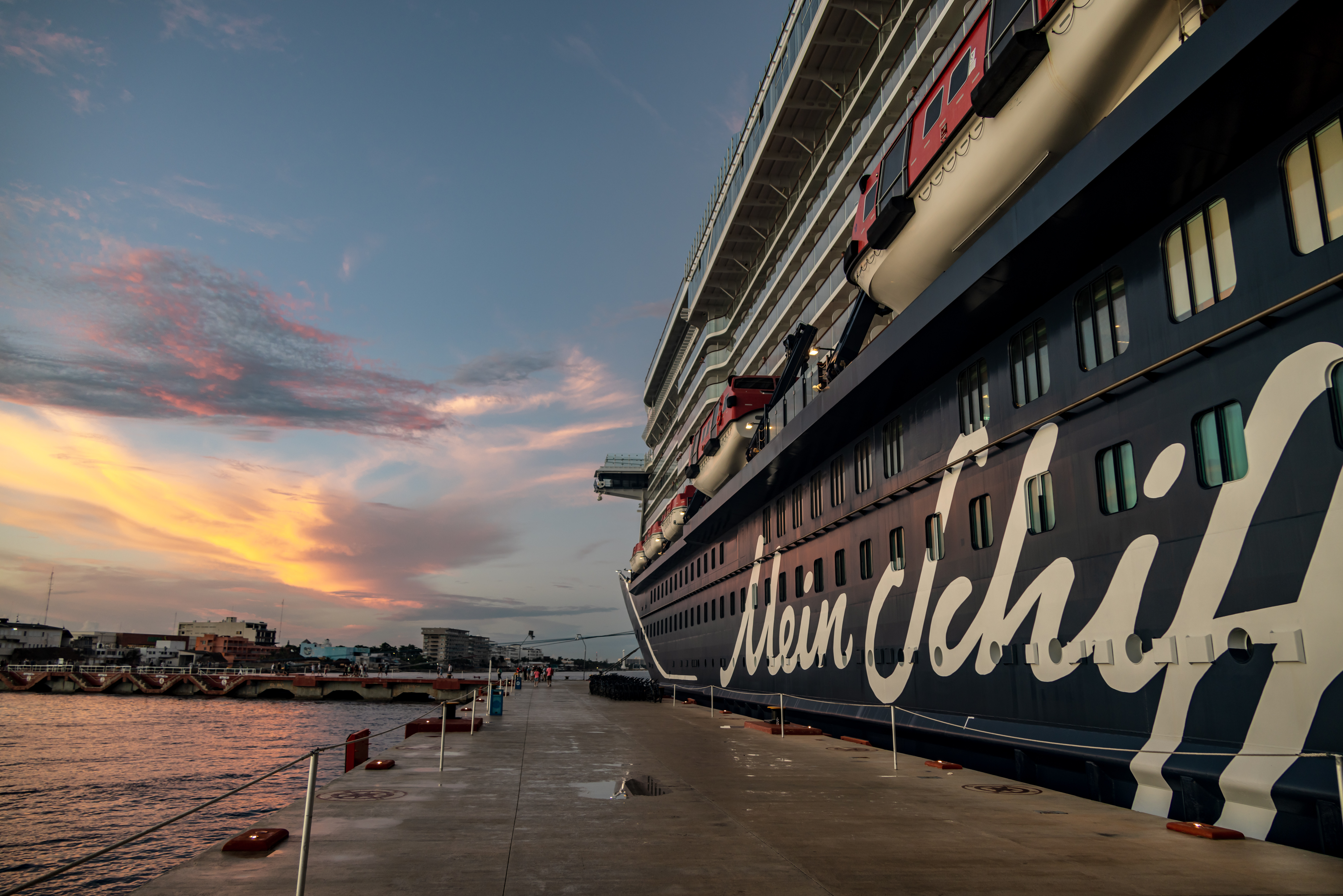 Kreuzfahrtschiff der Mein Schiff® Flotte bei Sonnenuntergang am Hafen.