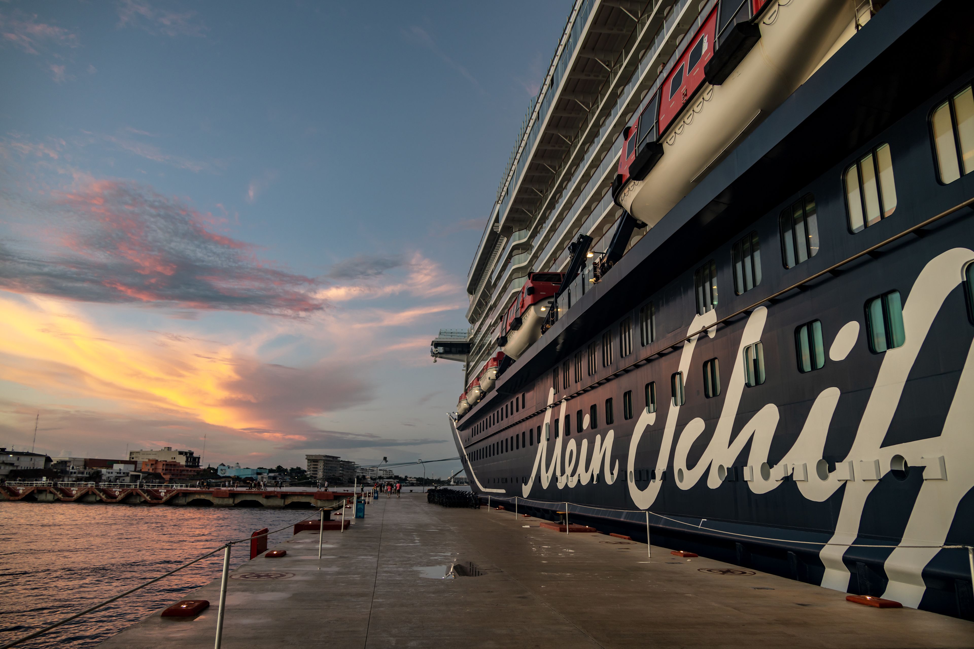 Kreuzfahrtschiff der Mein Schiff® Flotte bei Sonnenuntergang am Hafen.