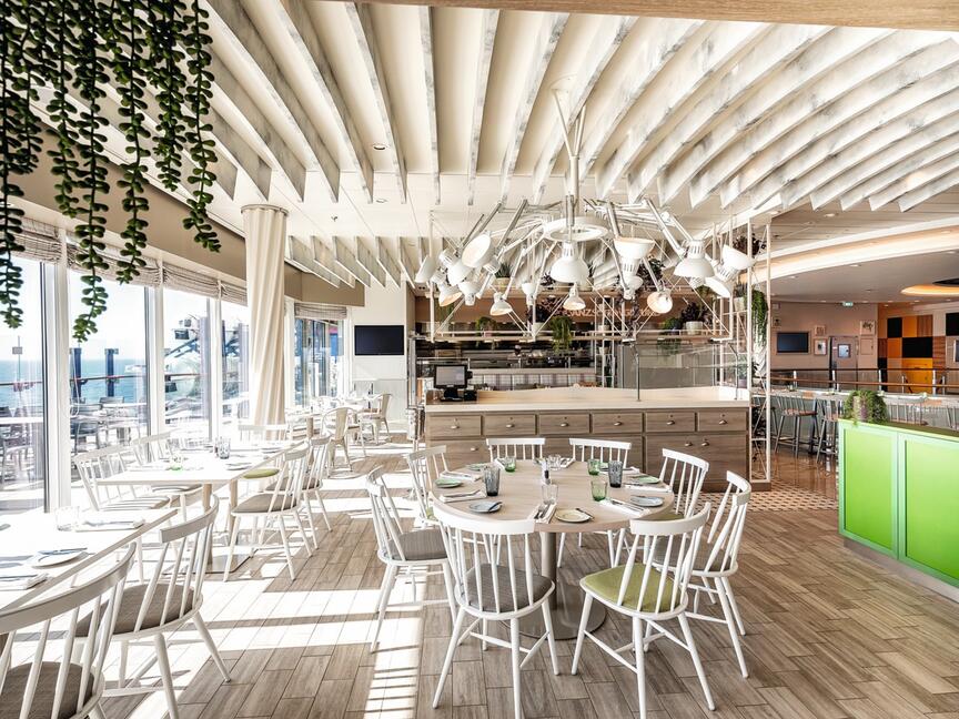 Helles Restaurant mit weißen Stühlen, Holzboden, grünen Akzenten.