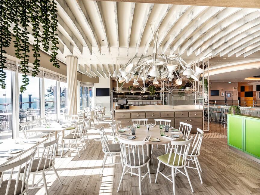 Helles Restaurant mit weißen Stühlen, Holzboden, grünen Akzenten.