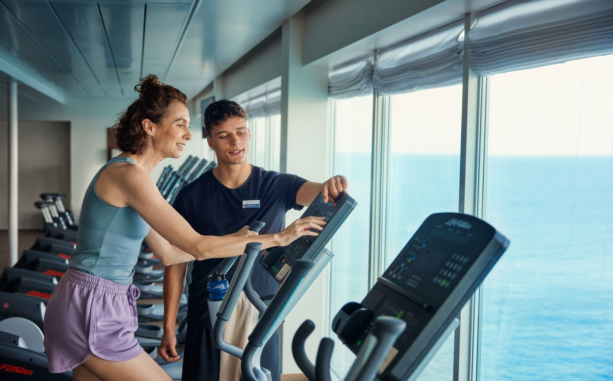 Frau und Trainer im Fitnessstudio auf Kreuzfahrtschiff mit Meerblick.
