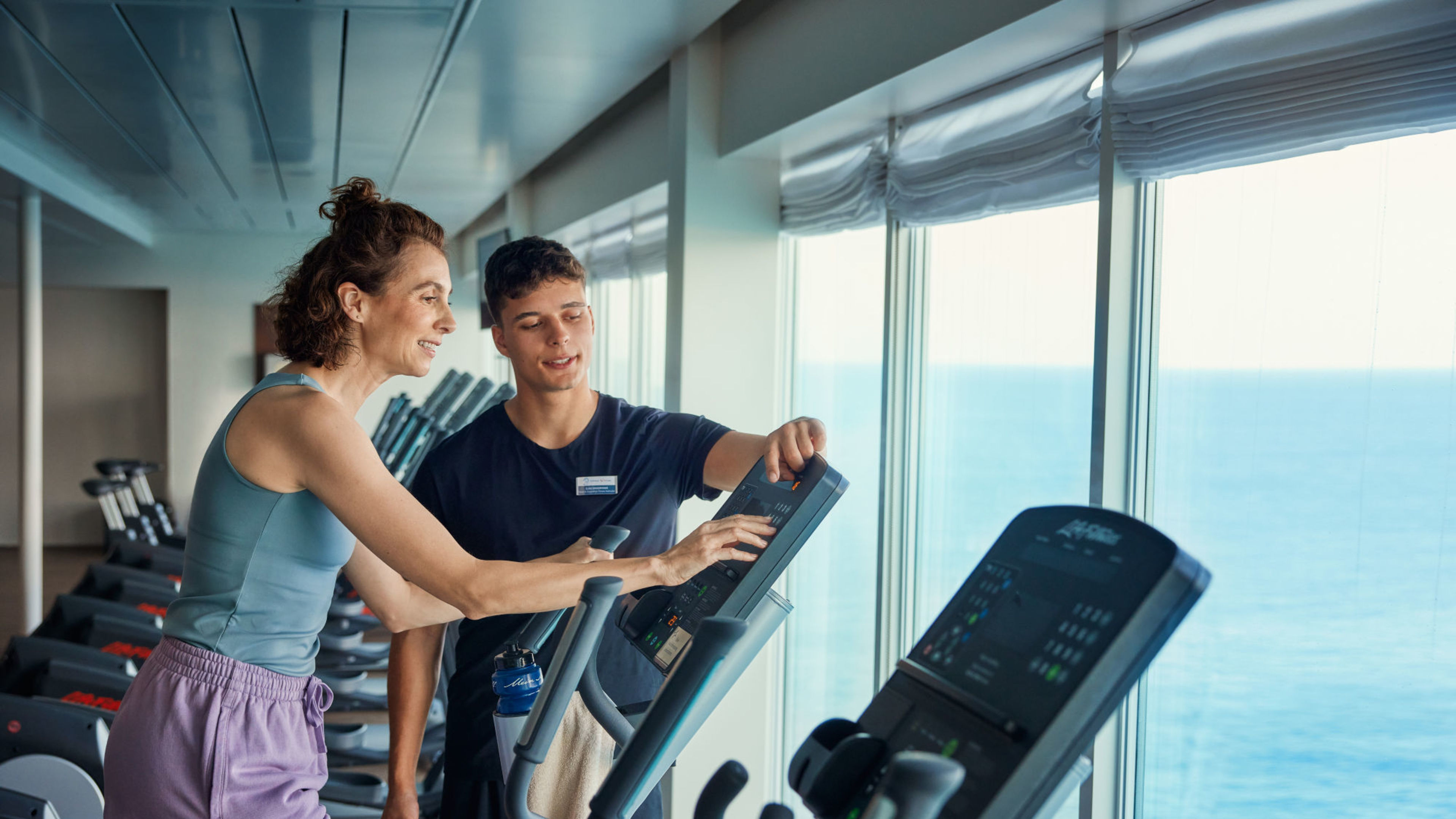 Sport & Fitnessbereich Frau und Trainer im Fitnessstudio auf Kreuzfahrtschiff mit Meerblick.
