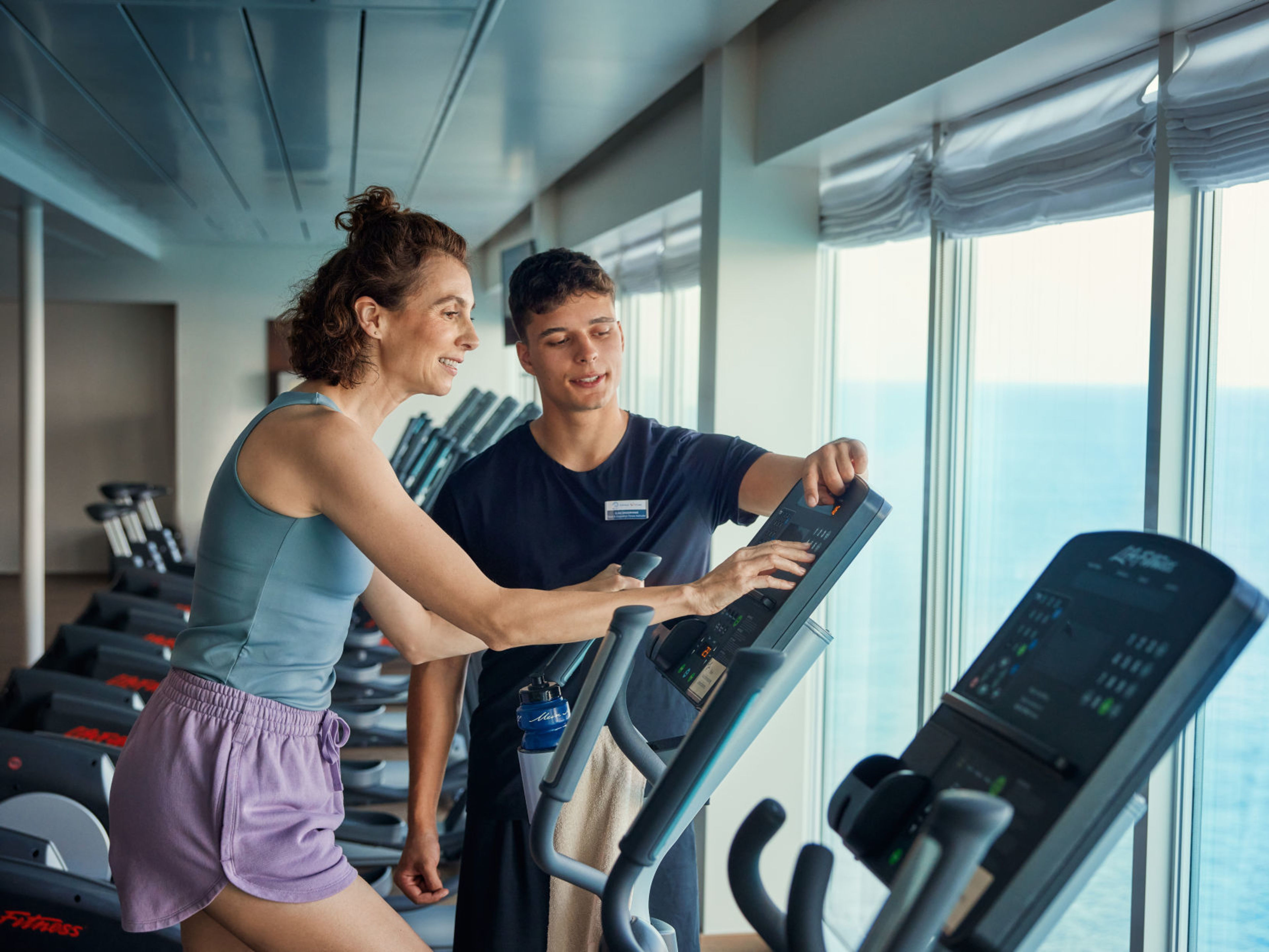 Sport & Fitnessbereich Frau und Trainer im Fitnessstudio auf Kreuzfahrtschiff mit Meerblick.