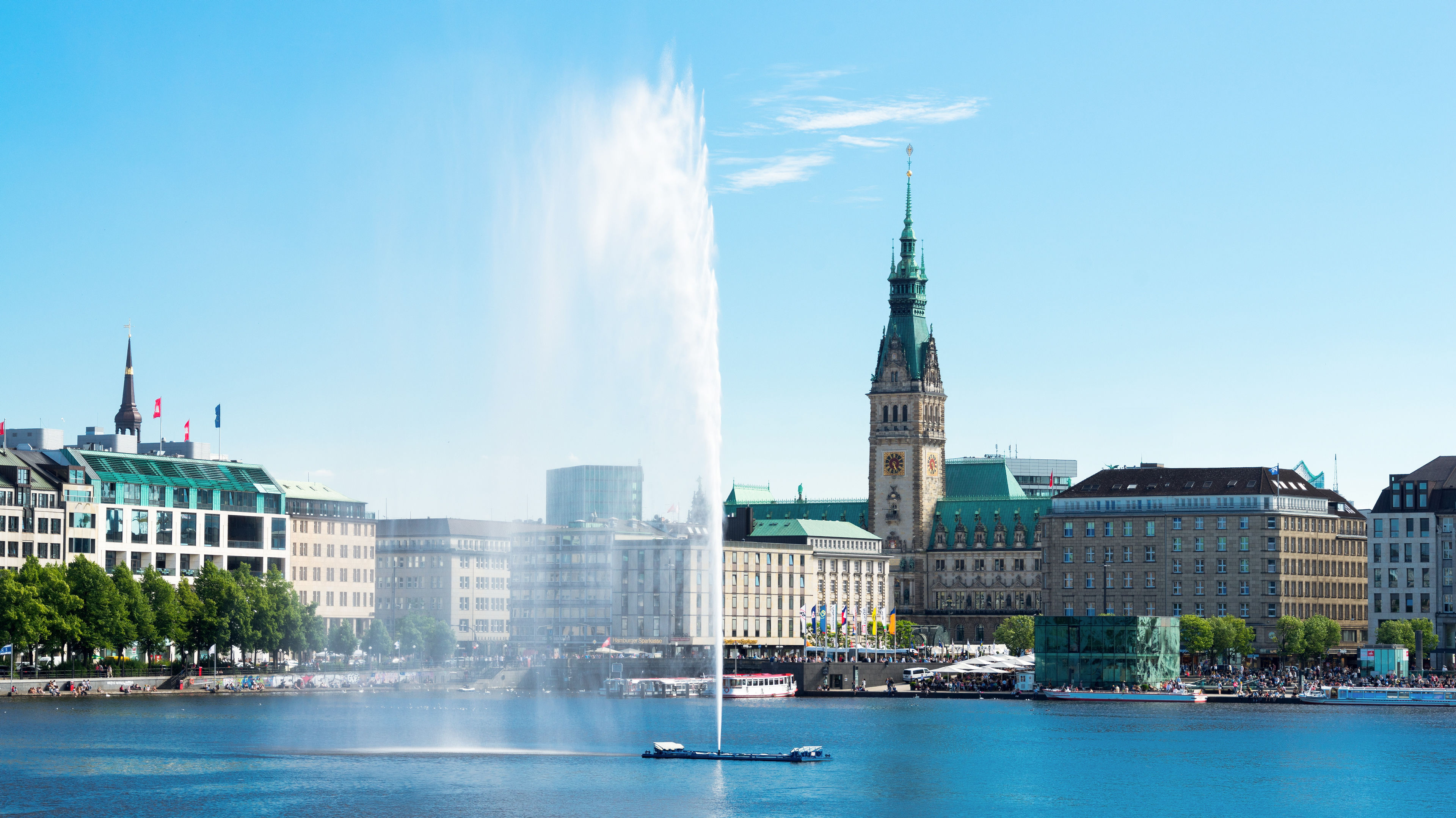 Hamburger Rathaus und Alsterfontäne bei klarem Himmel.