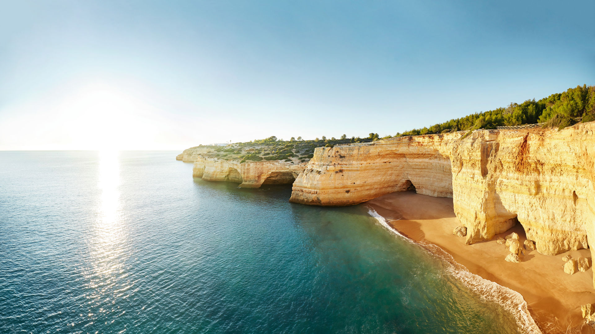 Küste der Algarve mit goldenen Klippen und blauem Meer.