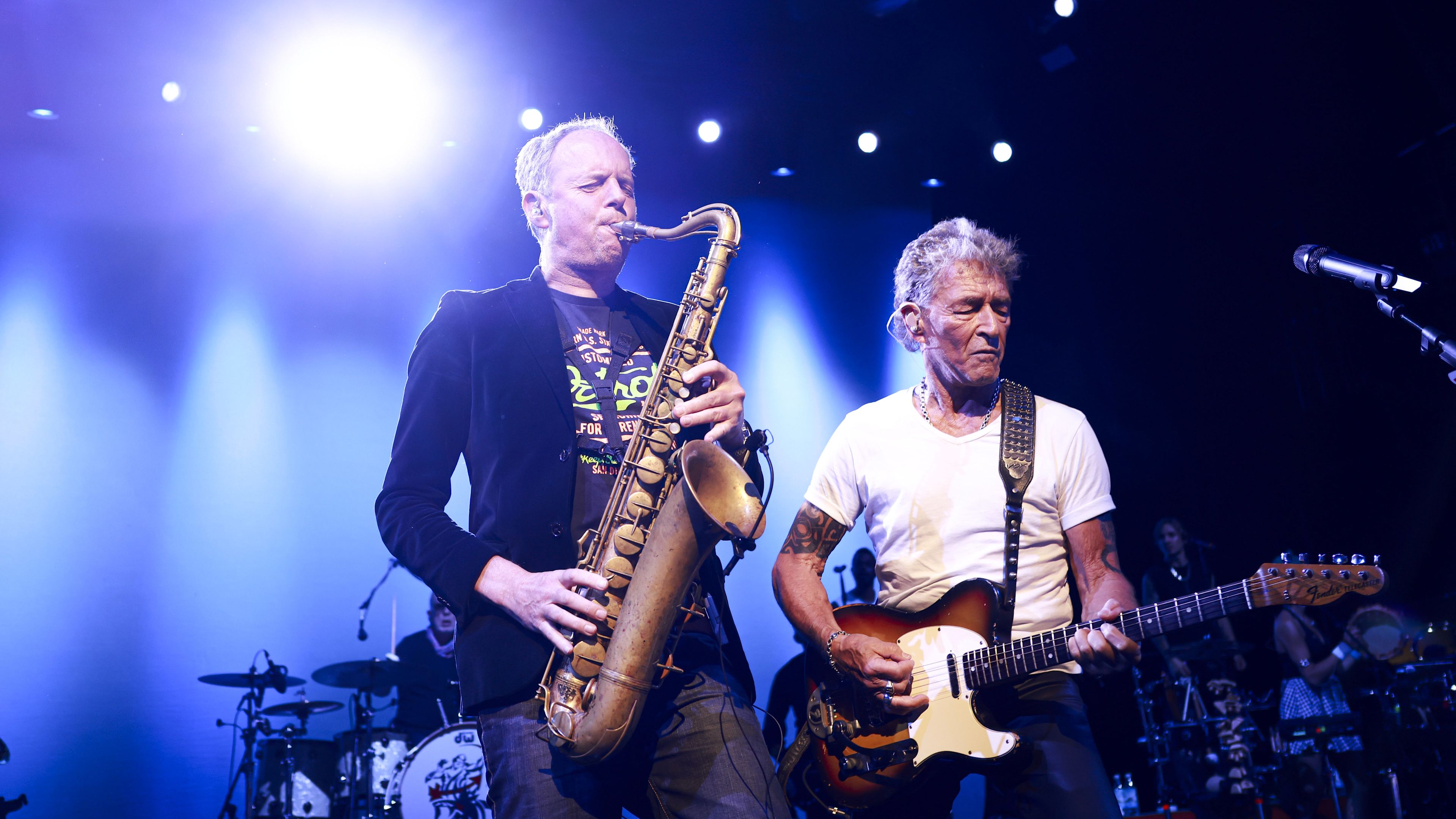 Musiker spielen Saxophon und Gitarre auf beleuchteter Bühne. Musiker spielen Saxophon und Gitarre auf beleuchteter Bühne.