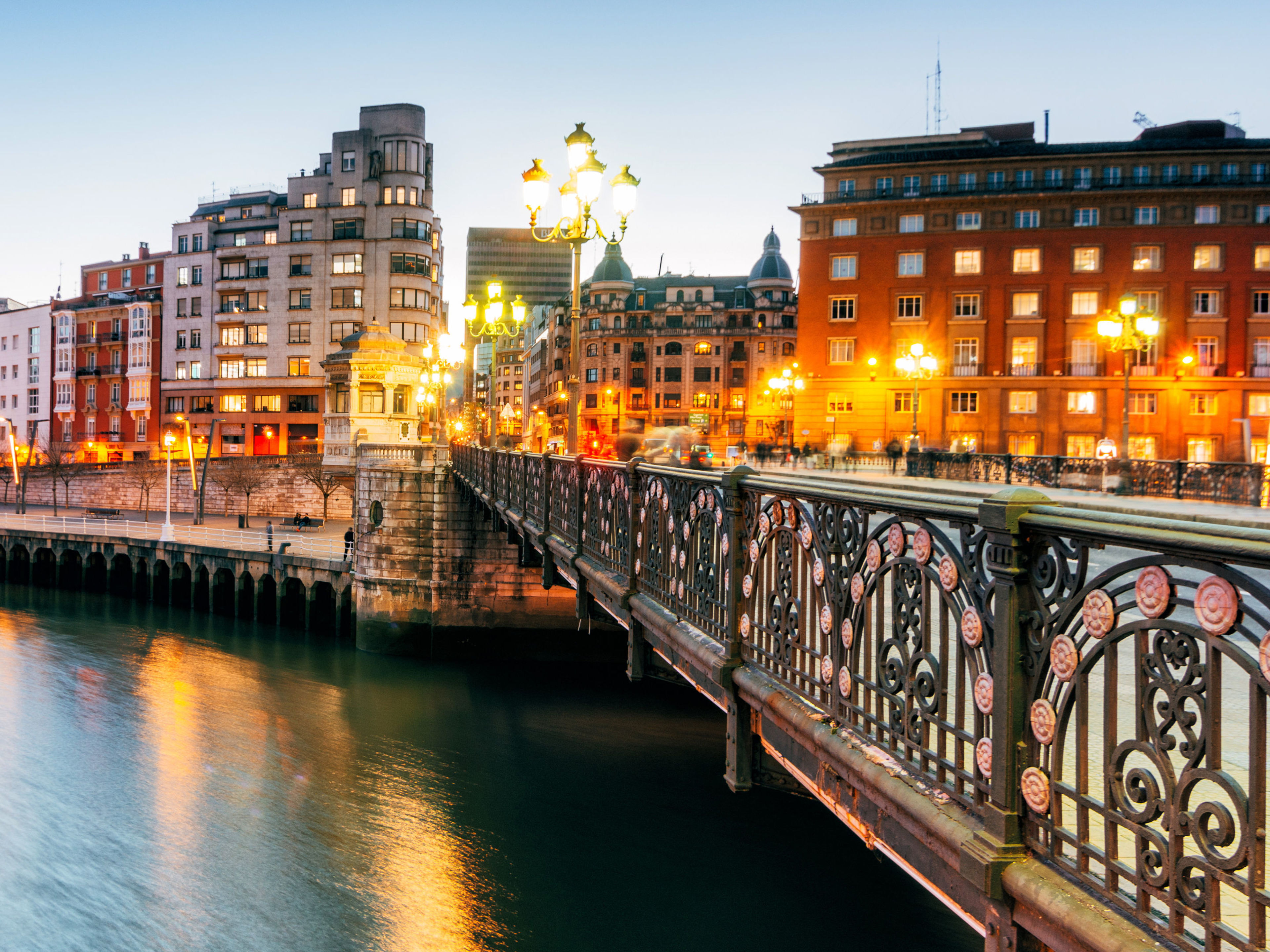 Bilbao Brücke und beleuchtete Gebäude am Flussufer in Bilbao bei Dämmerung.