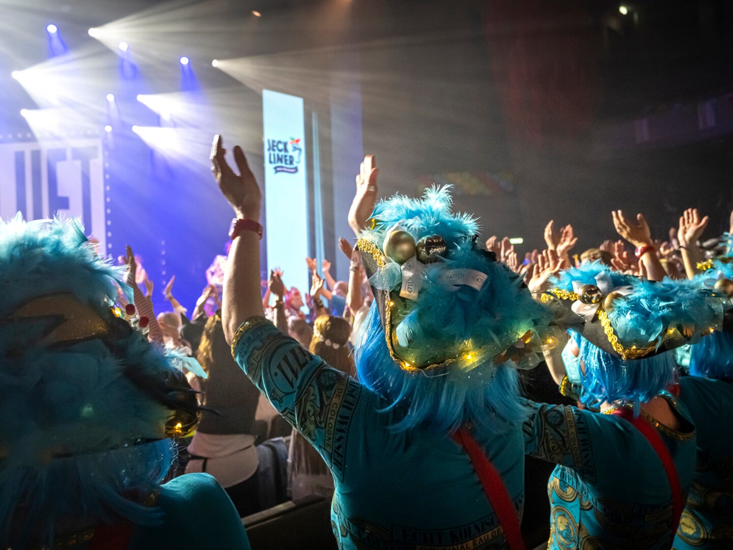 Menschen in blauen Kostümen feiern auf einer Bühne mit Lichtern.