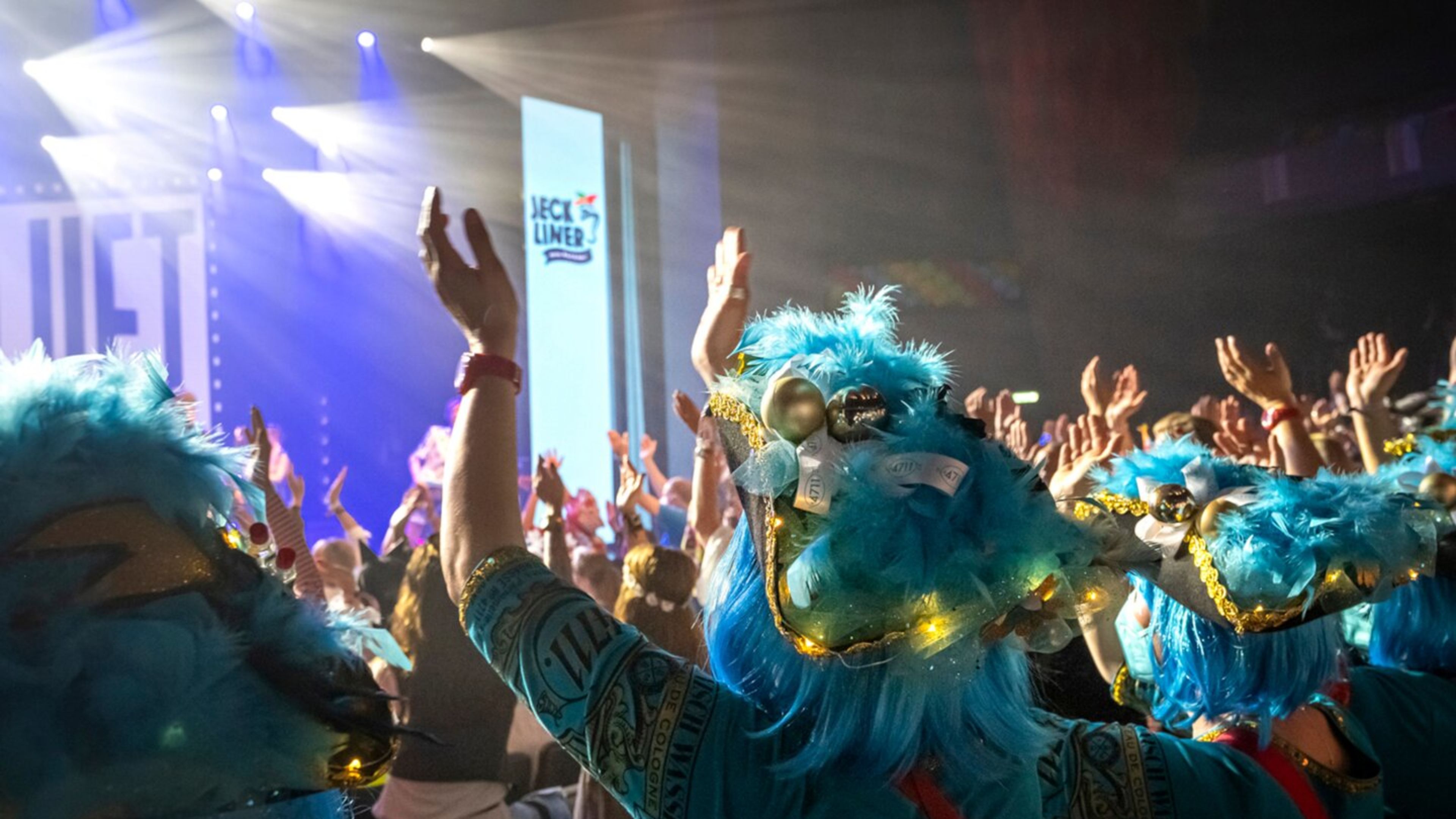 Jeckliner 4 Theater Menschen in blauen Kostümen feiern auf einer Bühne mit Lichtern.