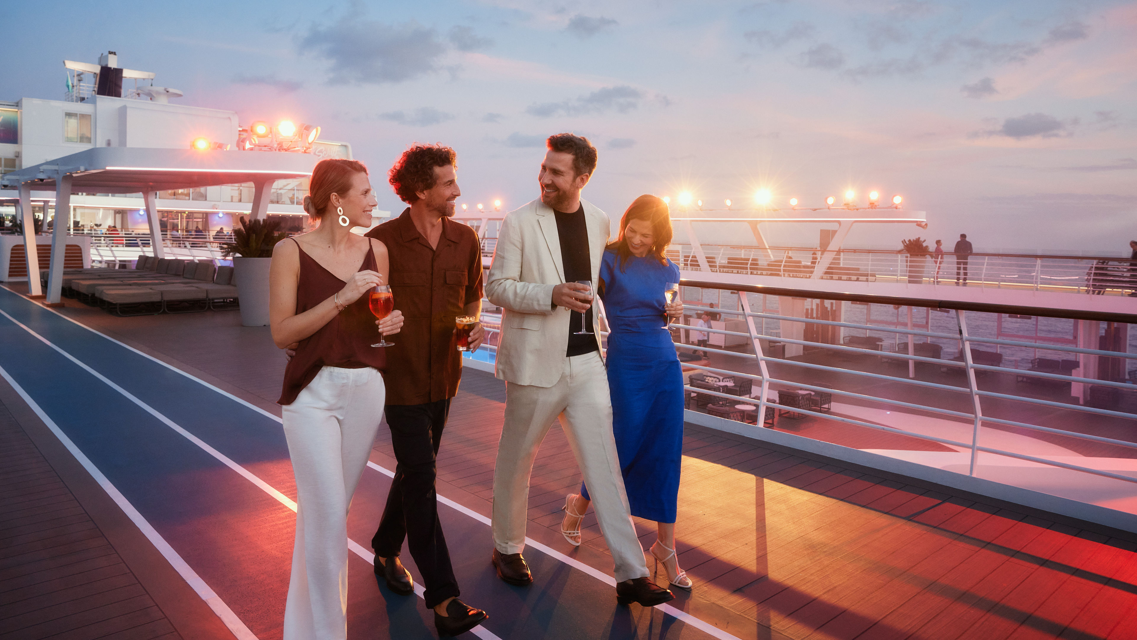 Vier Personen spazieren bei Sonnenuntergang auf einem Kreuzfahrtschiff der Mein Schiff® Flotte.