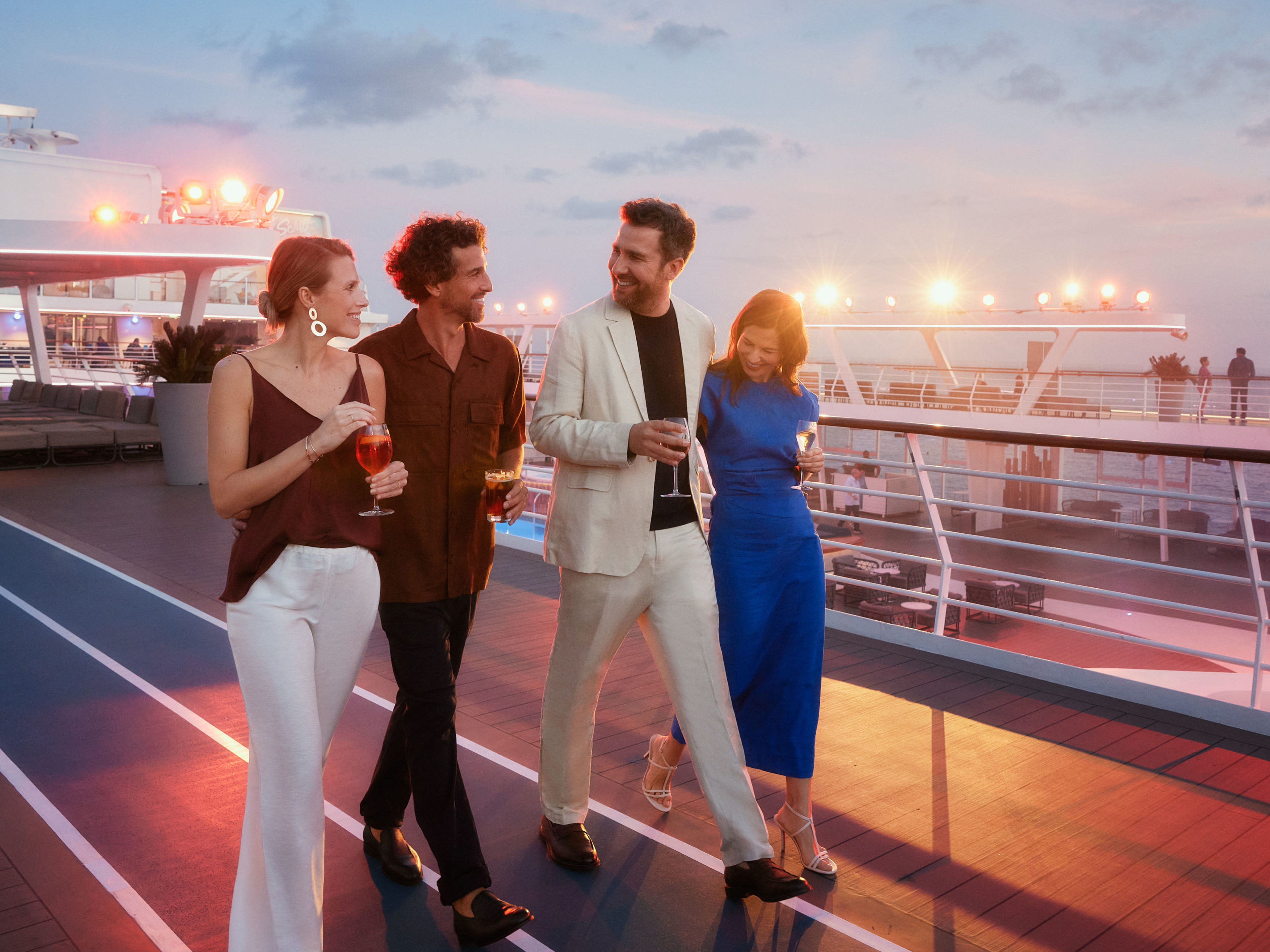 Freunde auf dem Weg zur Pool-Party Vier Personen spazieren bei Sonnenuntergang auf einem Kreuzfahrtschiff der Mein Schiff® Flotte.