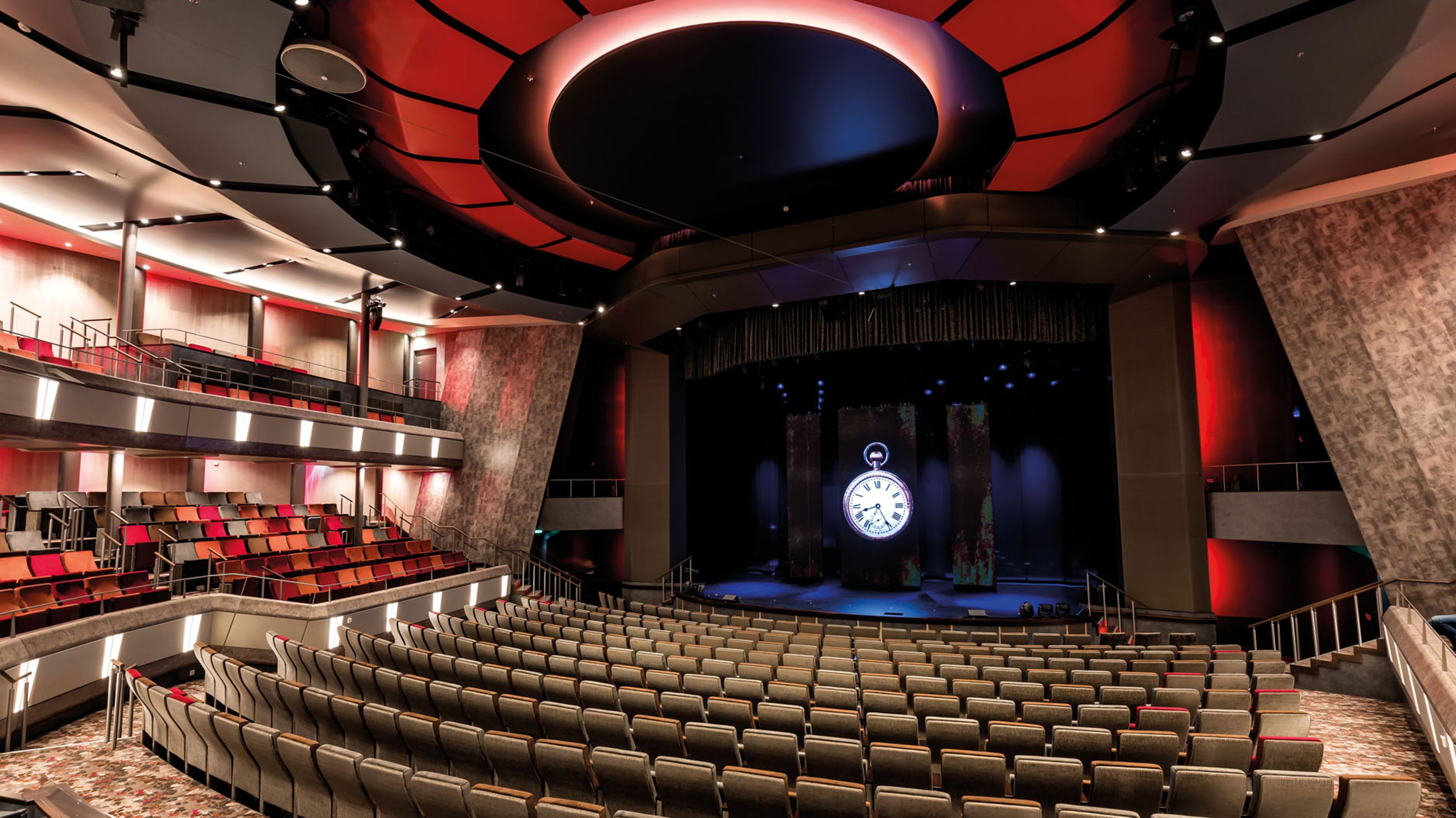 Leerer Theatersaal mit rotem Licht und großer Uhr auf der Bühne.