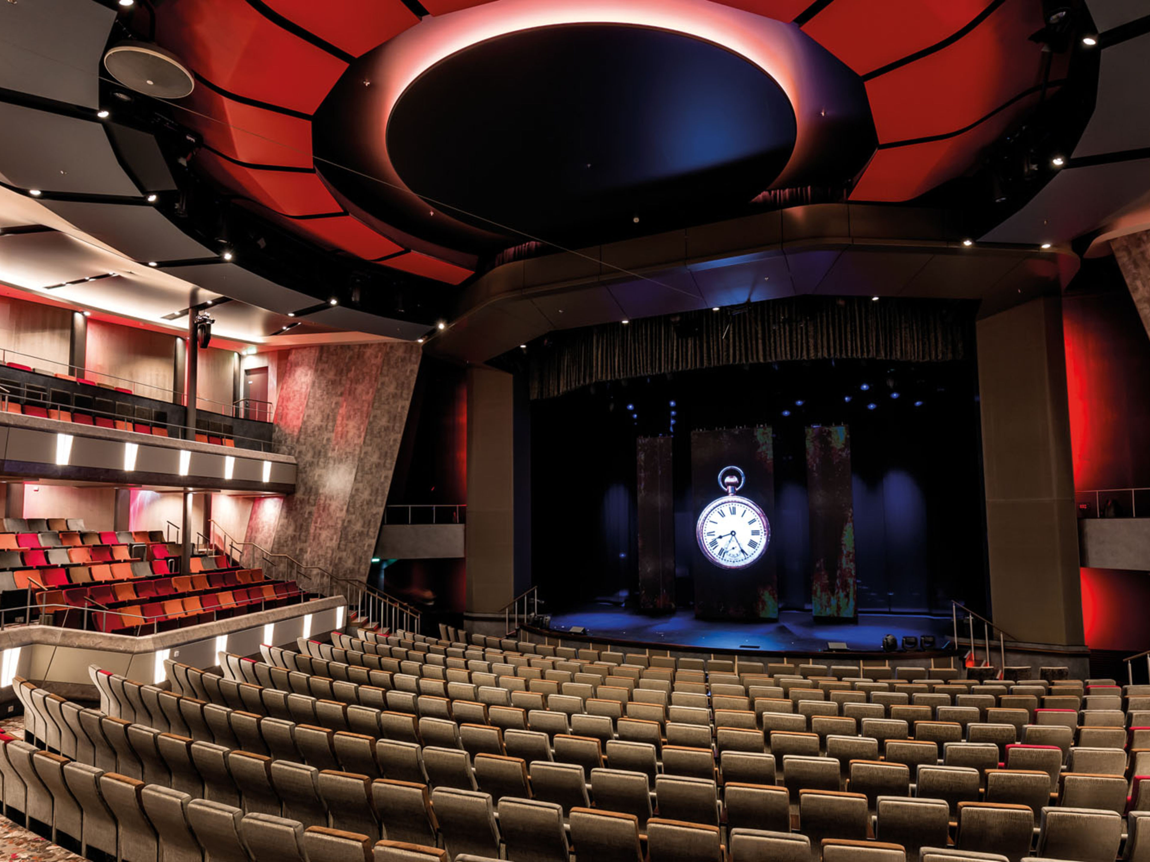 Leerer Theatersaal mit rotem Licht und großer Uhr auf der Bühne. Leerer Theatersaal mit rotem Licht und großer Uhr auf der Bühne.