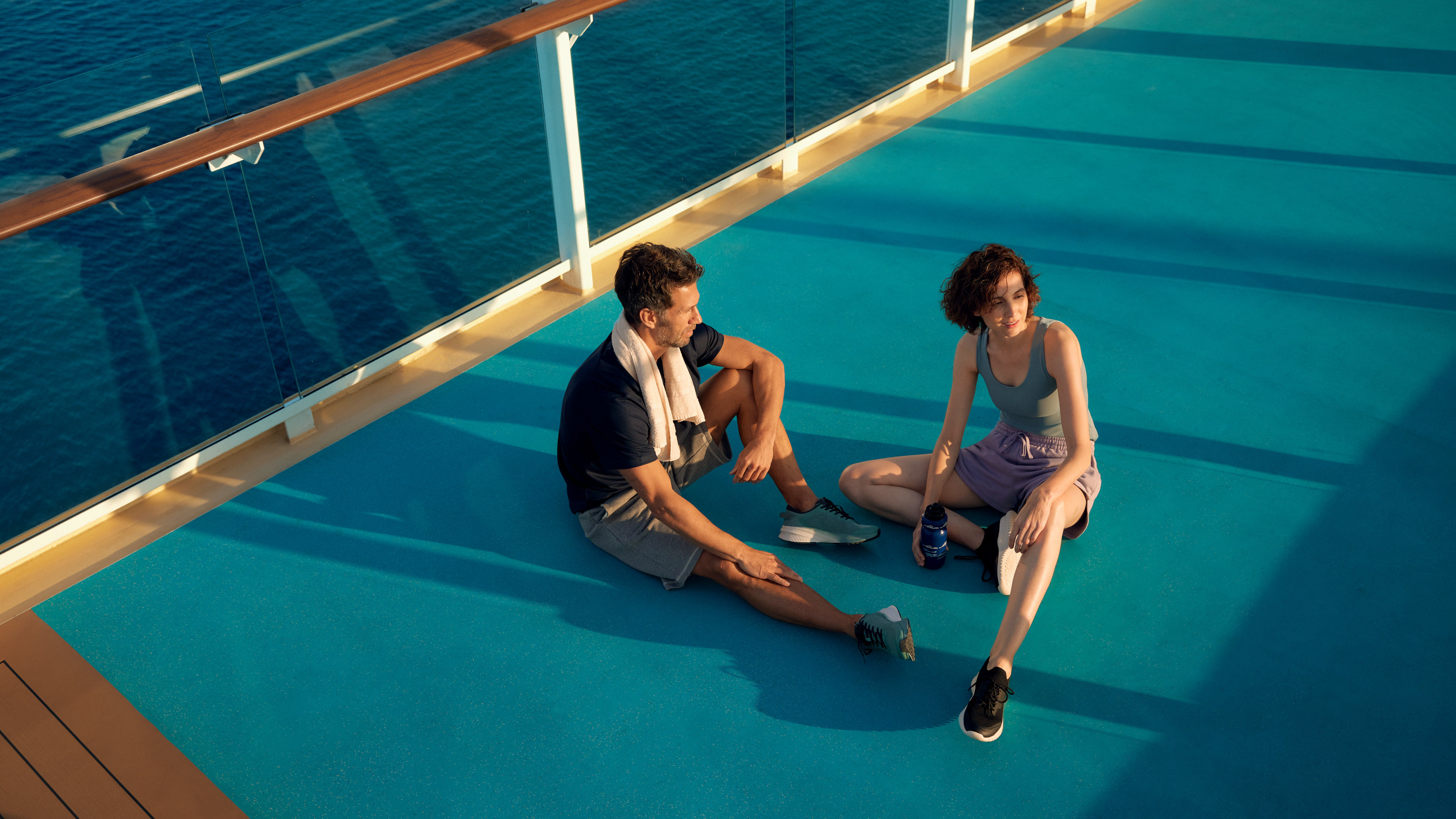 Zwei Personen entspannen auf dem Deck eines Kreuzfahrtschiffs bei Sonnenuntergang.