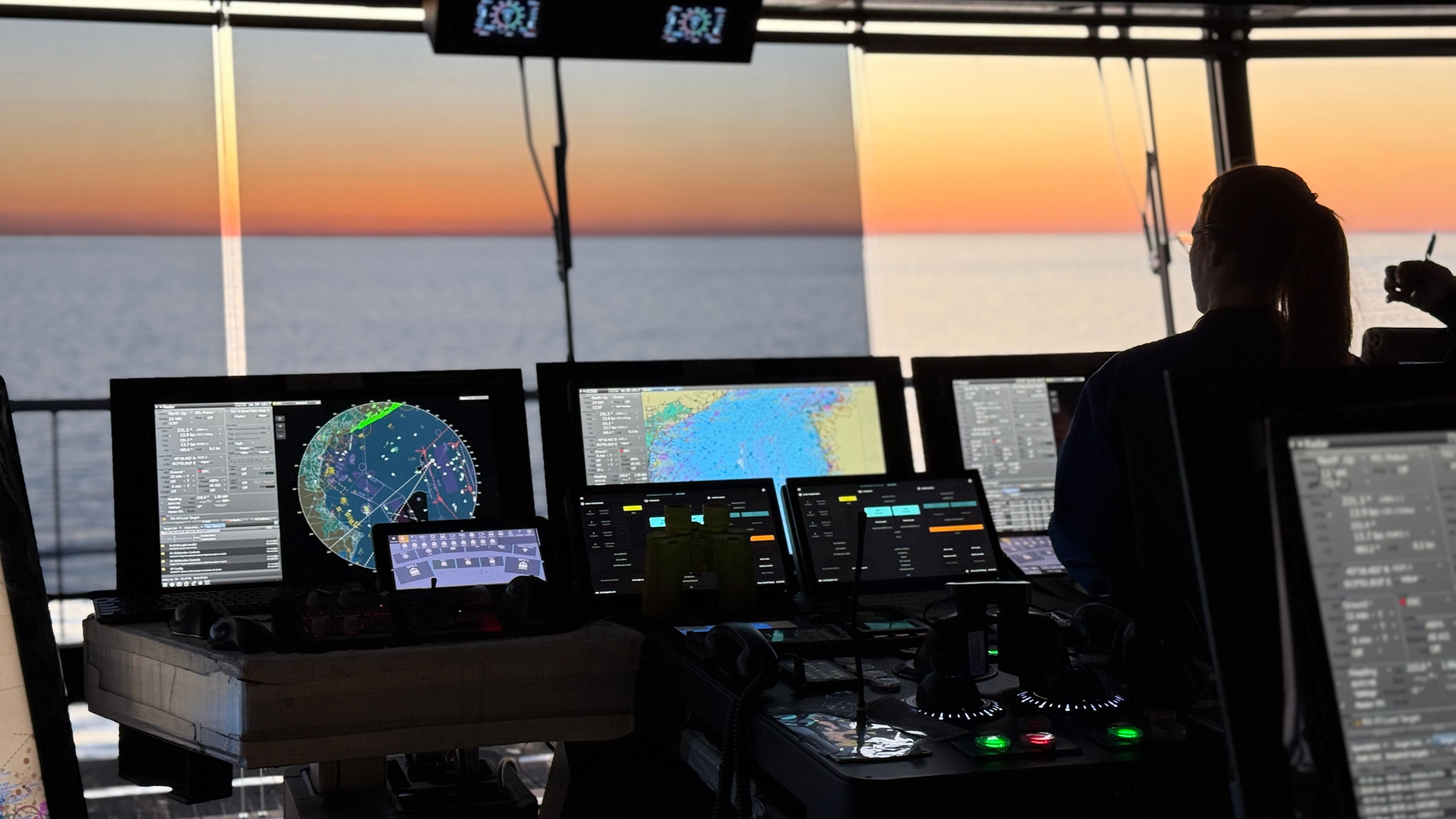 Brücke Mein Schiff 7 Person auf Brücke eines Kreuzfahrtschiffs bei Sonnenuntergang, Bildschirme leuchten.