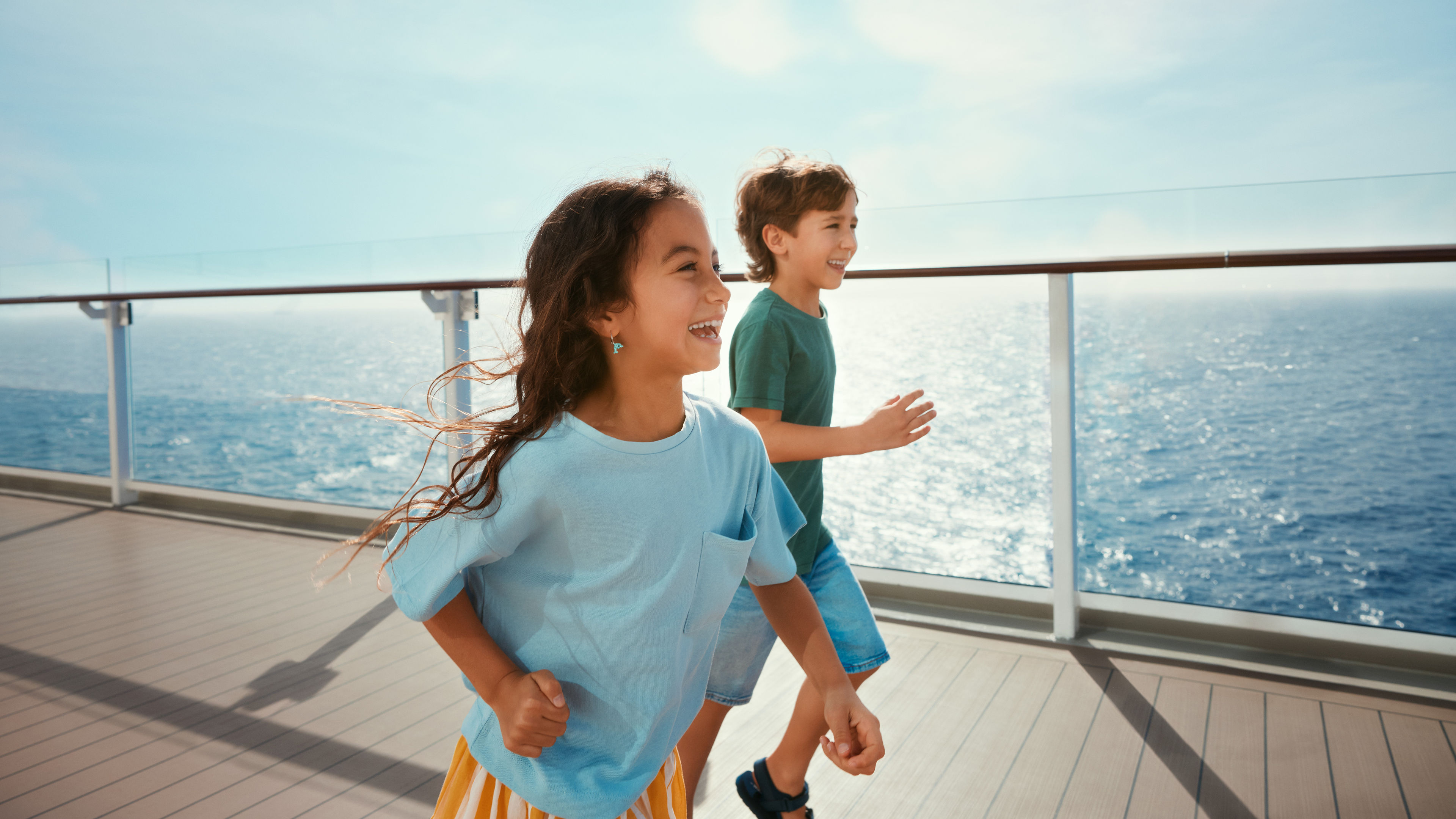Kinder laufen lachend auf Kreuzfahrtschiff der Mein Schiff® Flotte, Meer im Hintergrund.
