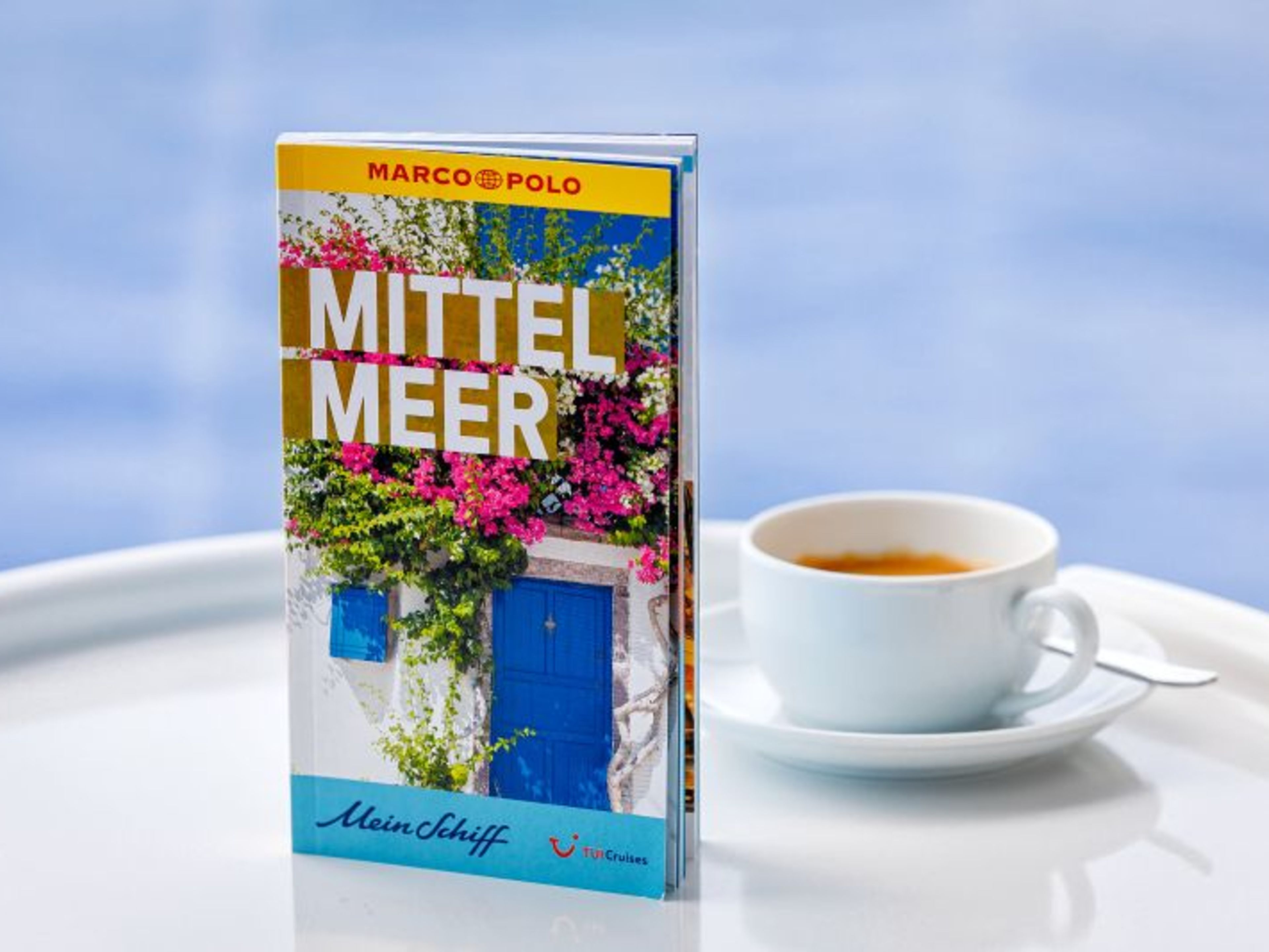 Marco Polo Reiseführer Reiseführer "Mittelmeer" neben einer Tasse Kaffee auf weißem Tisch.