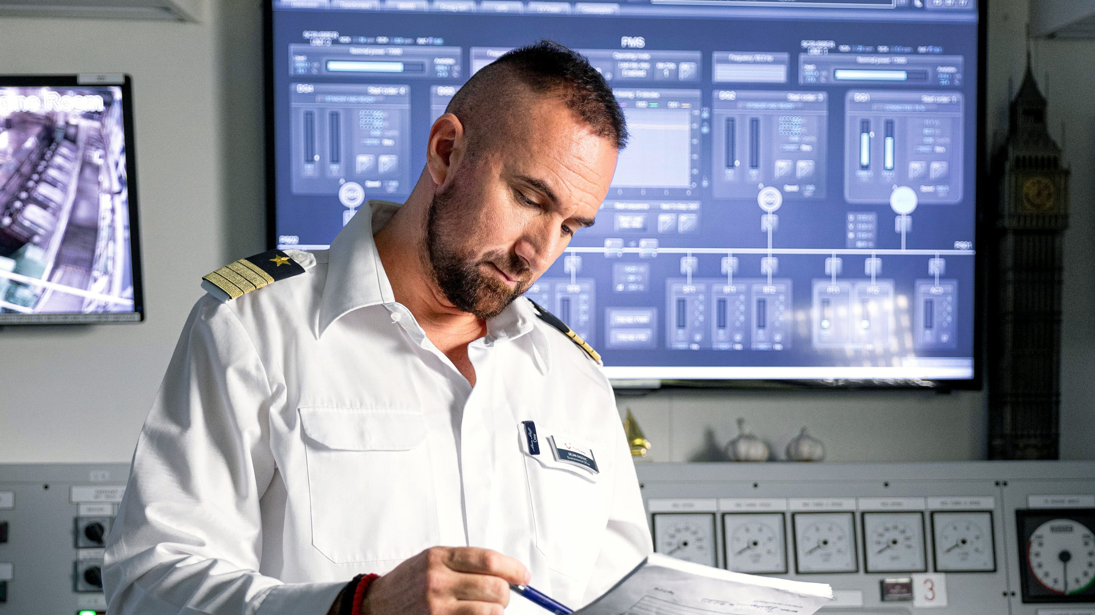 Mann in Uniform liest Dokumente vor Bildschirmen.