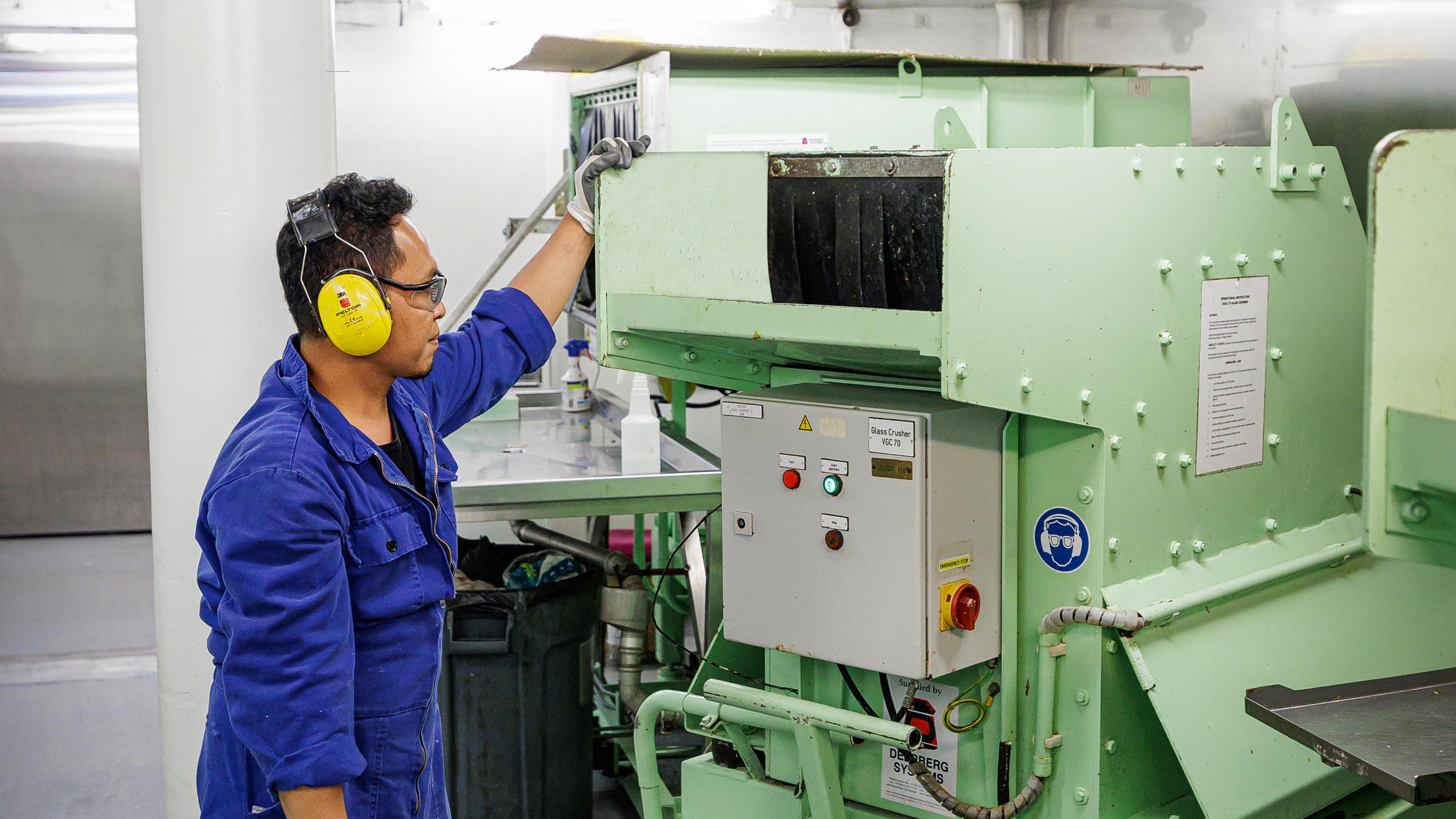 Mann in blauer Arbeitskleidung bedient grüne Maschine.