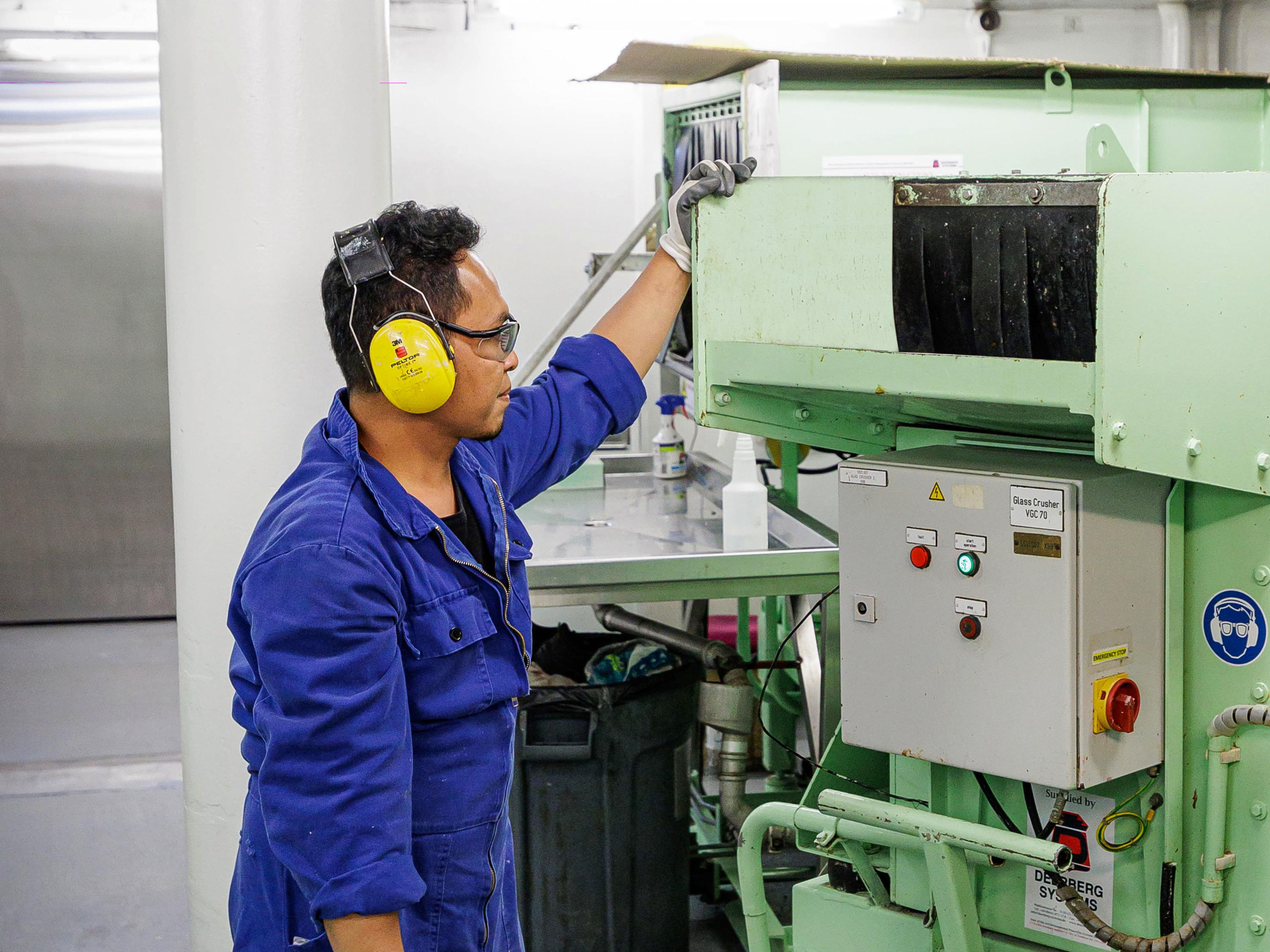 Nachhaltigkeit - Abfallmanagement - Mülltrennung Mann in blauer Arbeitskleidung bedient grüne Maschine.