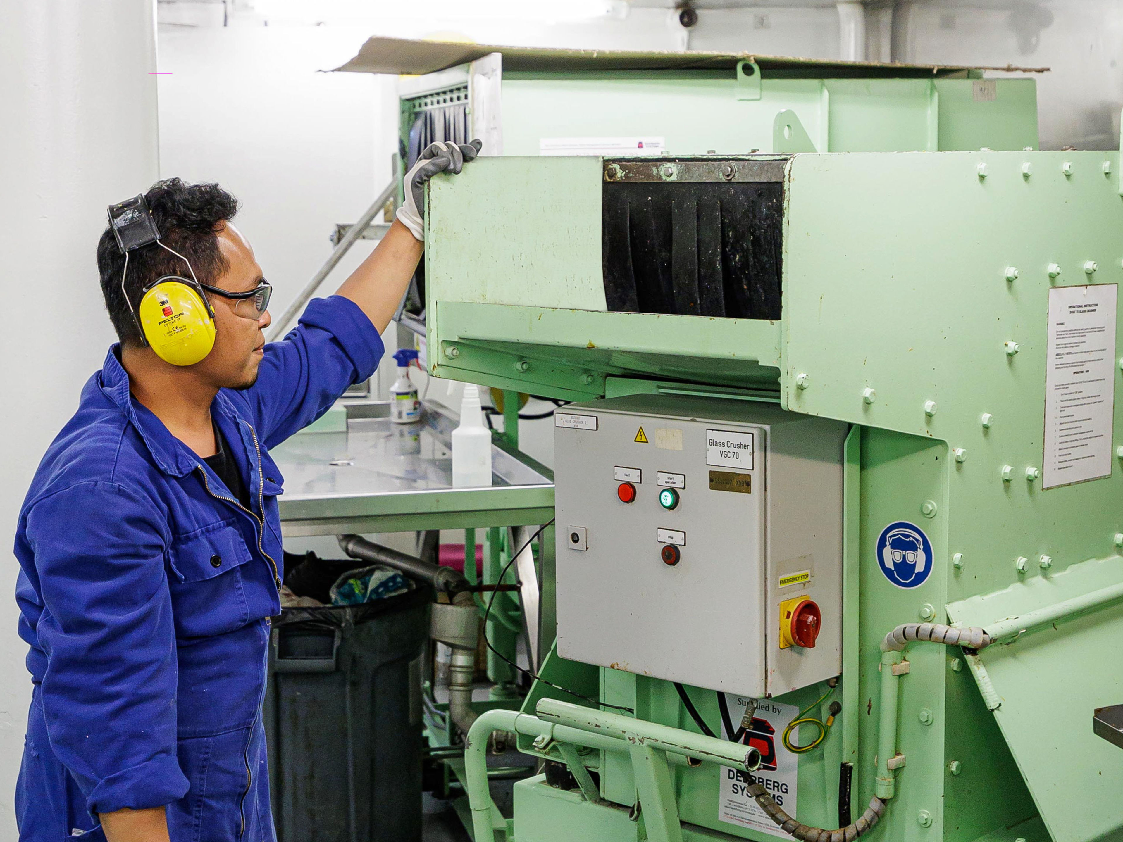 Mann in blauer Arbeitskleidung bedient grüne Maschine. Mann in blauer Arbeitskleidung bedient grüne Maschine.