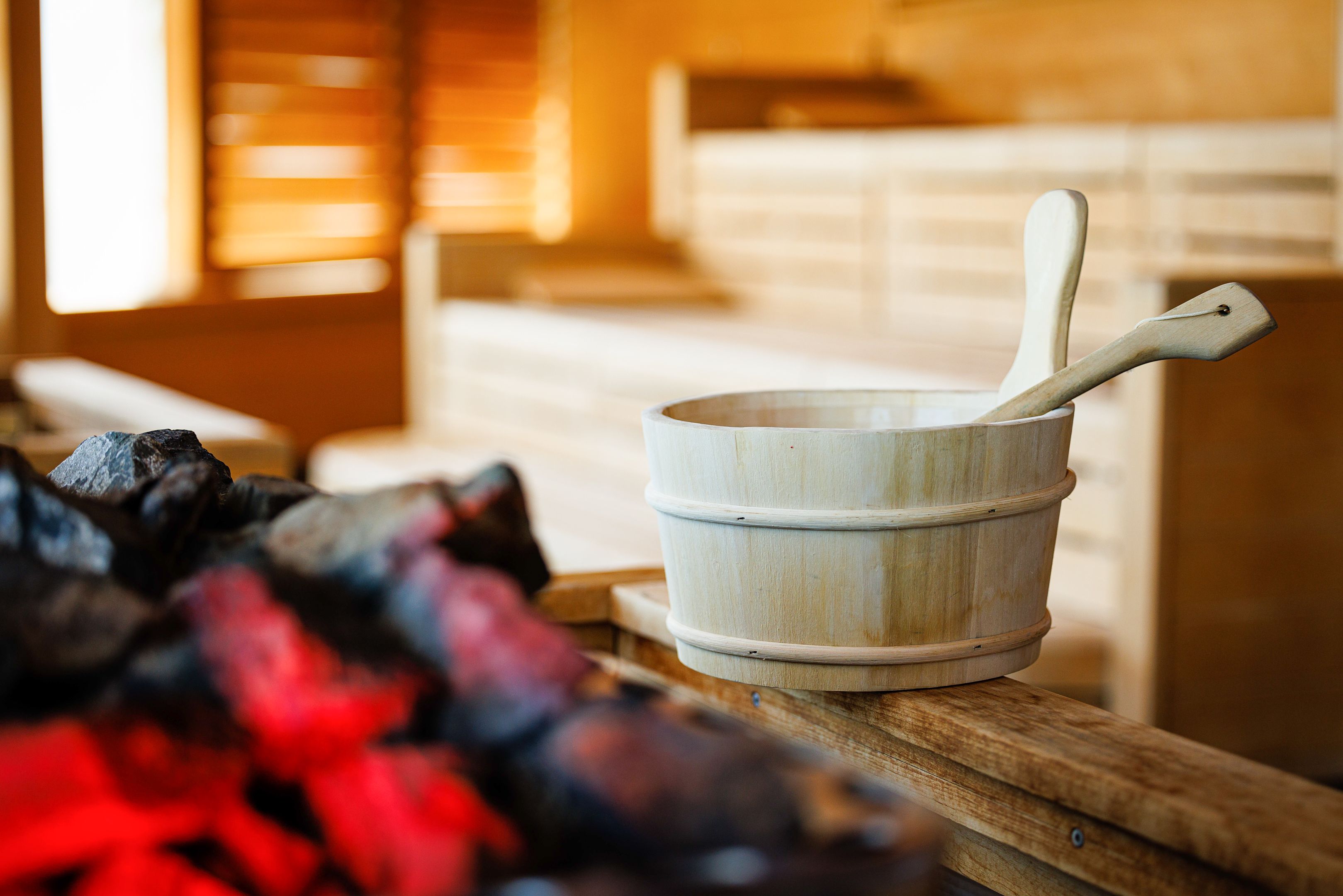 Holzeimer und Schöpfkelle in einer Sauna mit heißen Steinen.
