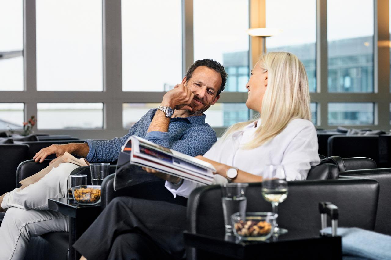 Paar entspannt in Lounge, liest Magazin, trinkt Wein.