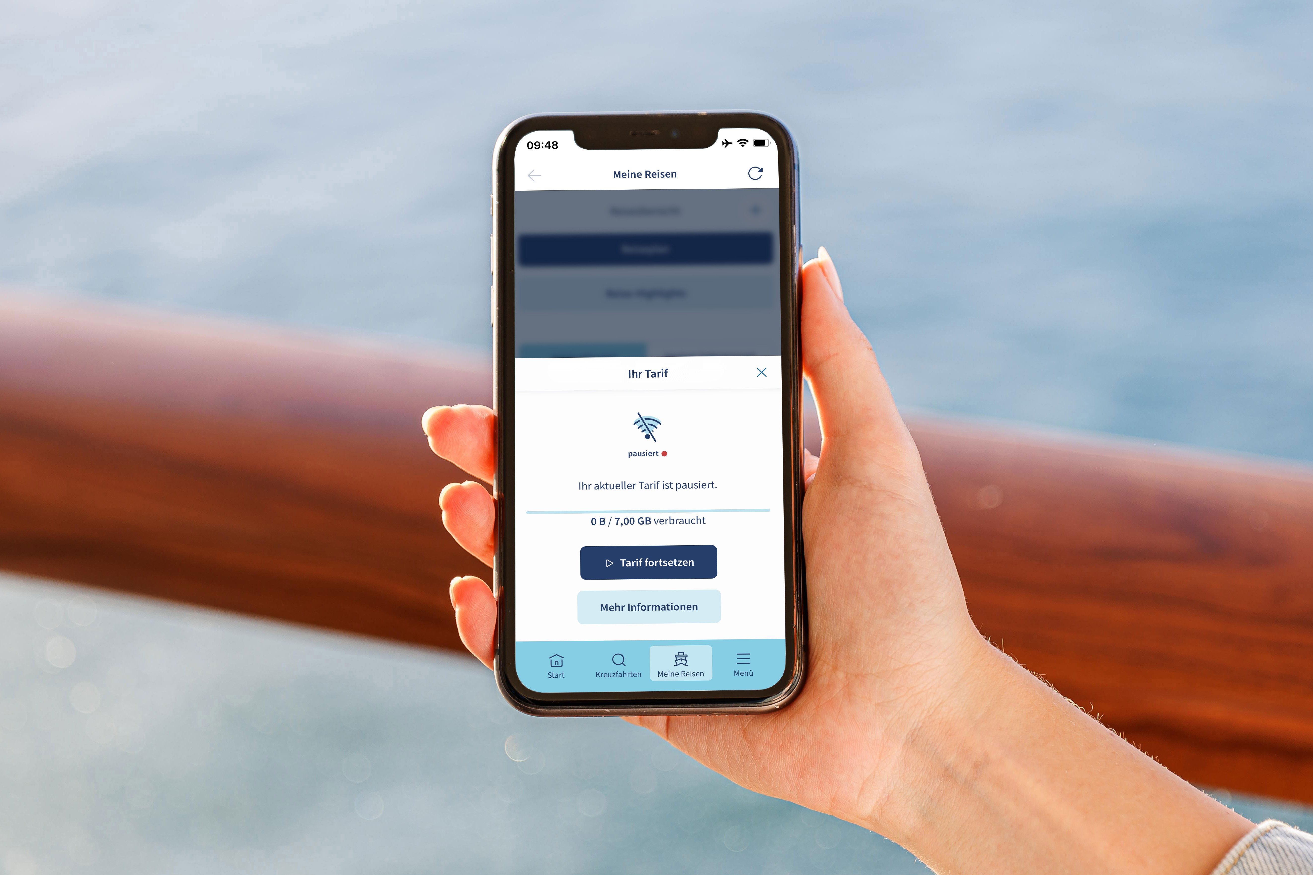 Hand hält Smartphone mit App, Meer im Hintergrund.